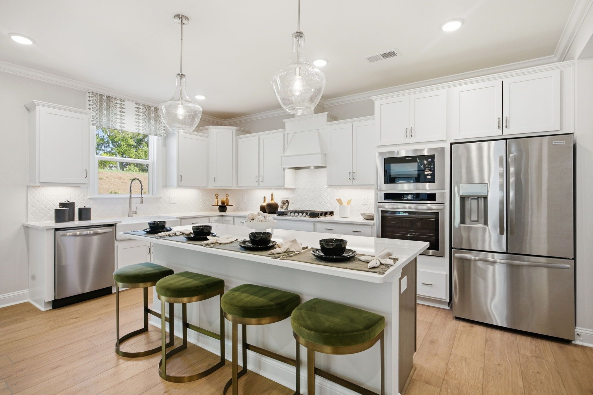 Spacious white kitchen with island, green velvet stools, stainless fridge and dishwasher at Enclave at Belmont, NC