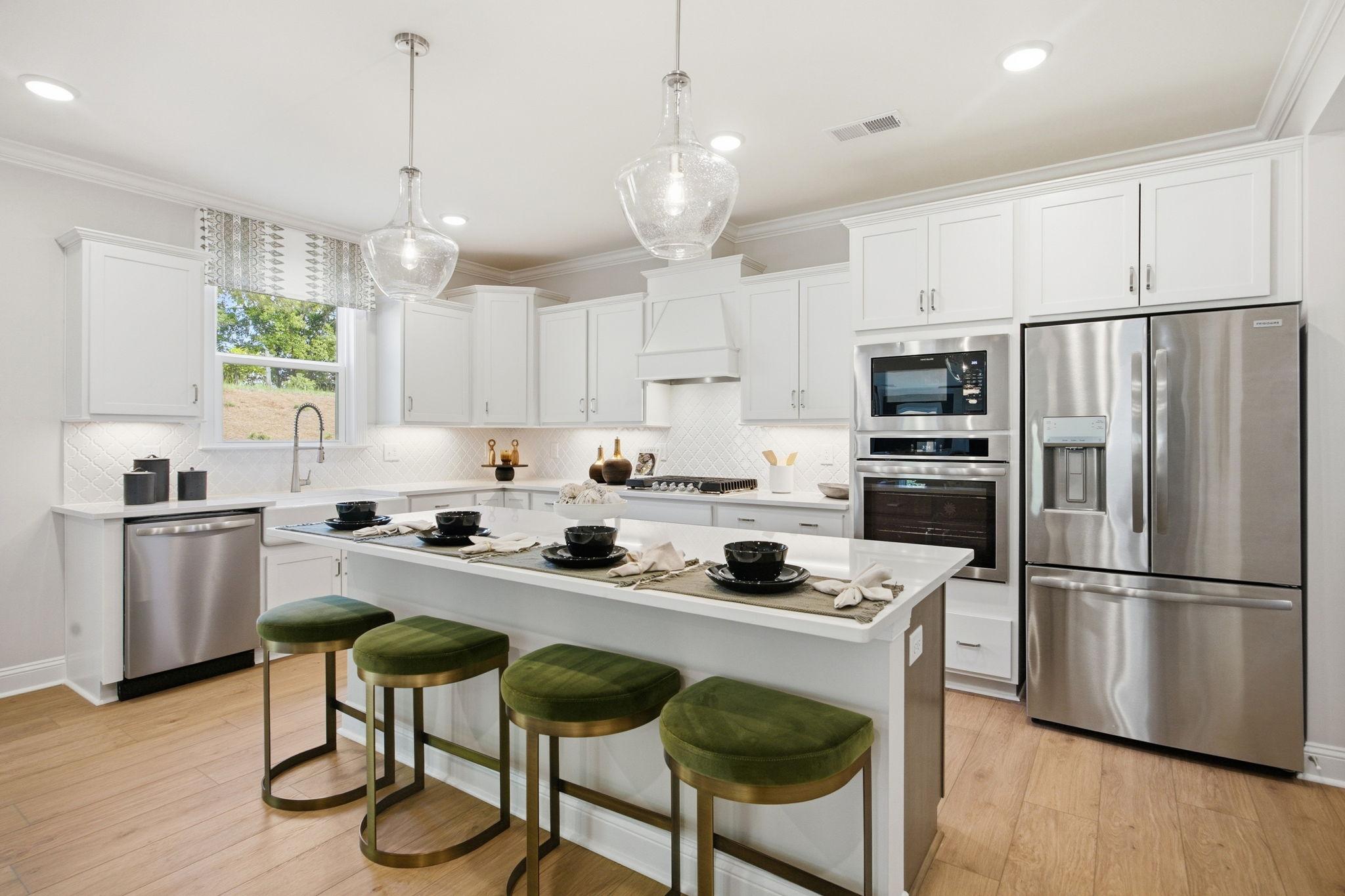 Spacious white kitchen with island, green velvet stools, stainless fridge and dishwasher at Enclave at Belmont, NC