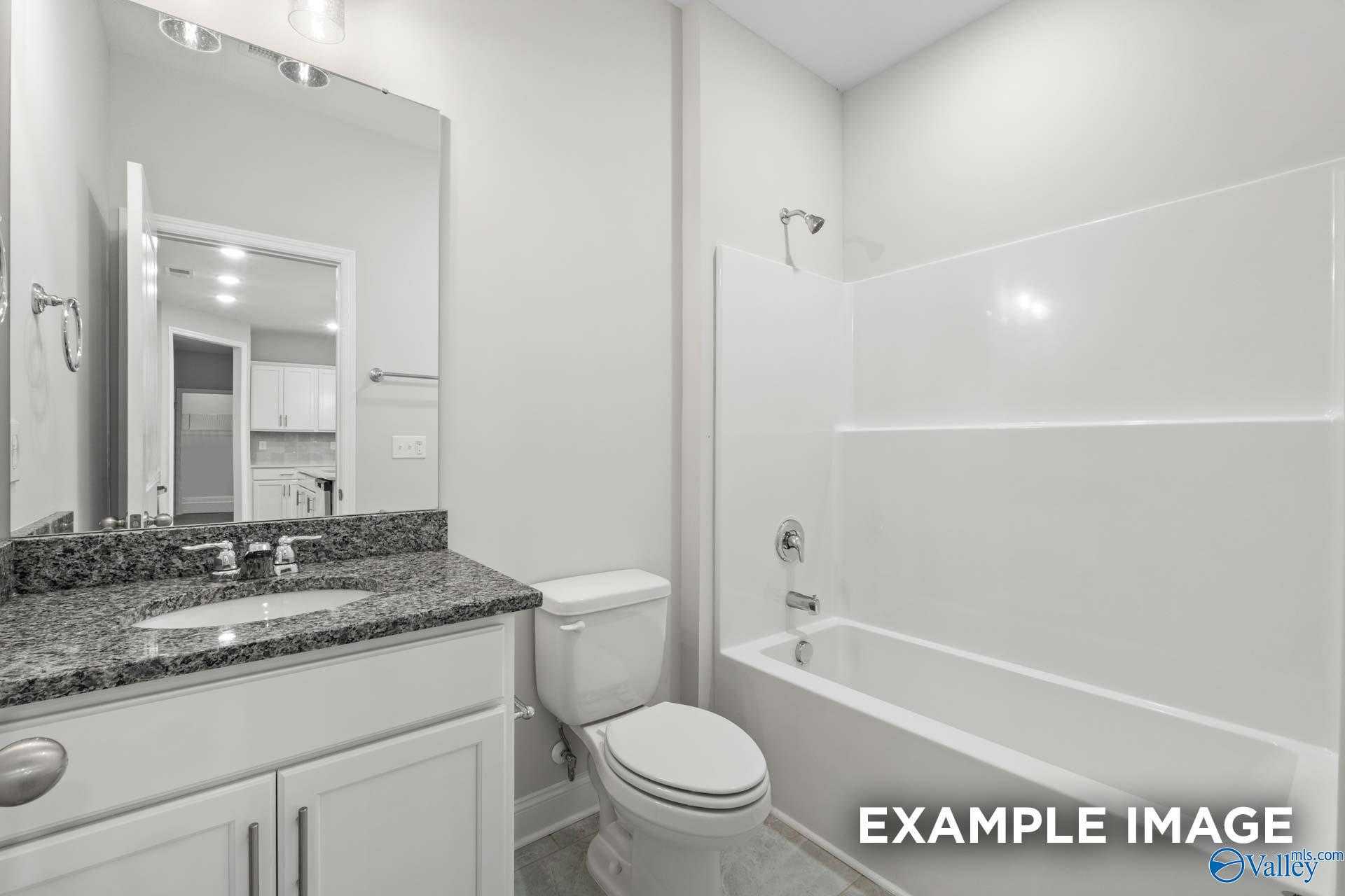 Modern bathroom with granite vanity, white tub-shower combo, mirror and toilet in The Lanier floor plan, Davidson Homes, Meridianville, Alabama