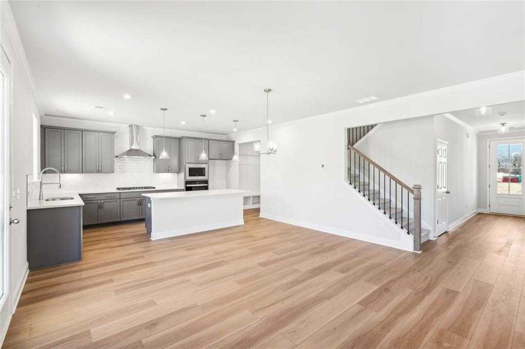 Open-concept kitchen with gray cabinets, stainless appliances, white island, hardwood floors, and staircase in The Hickory C, Hoschton, GA