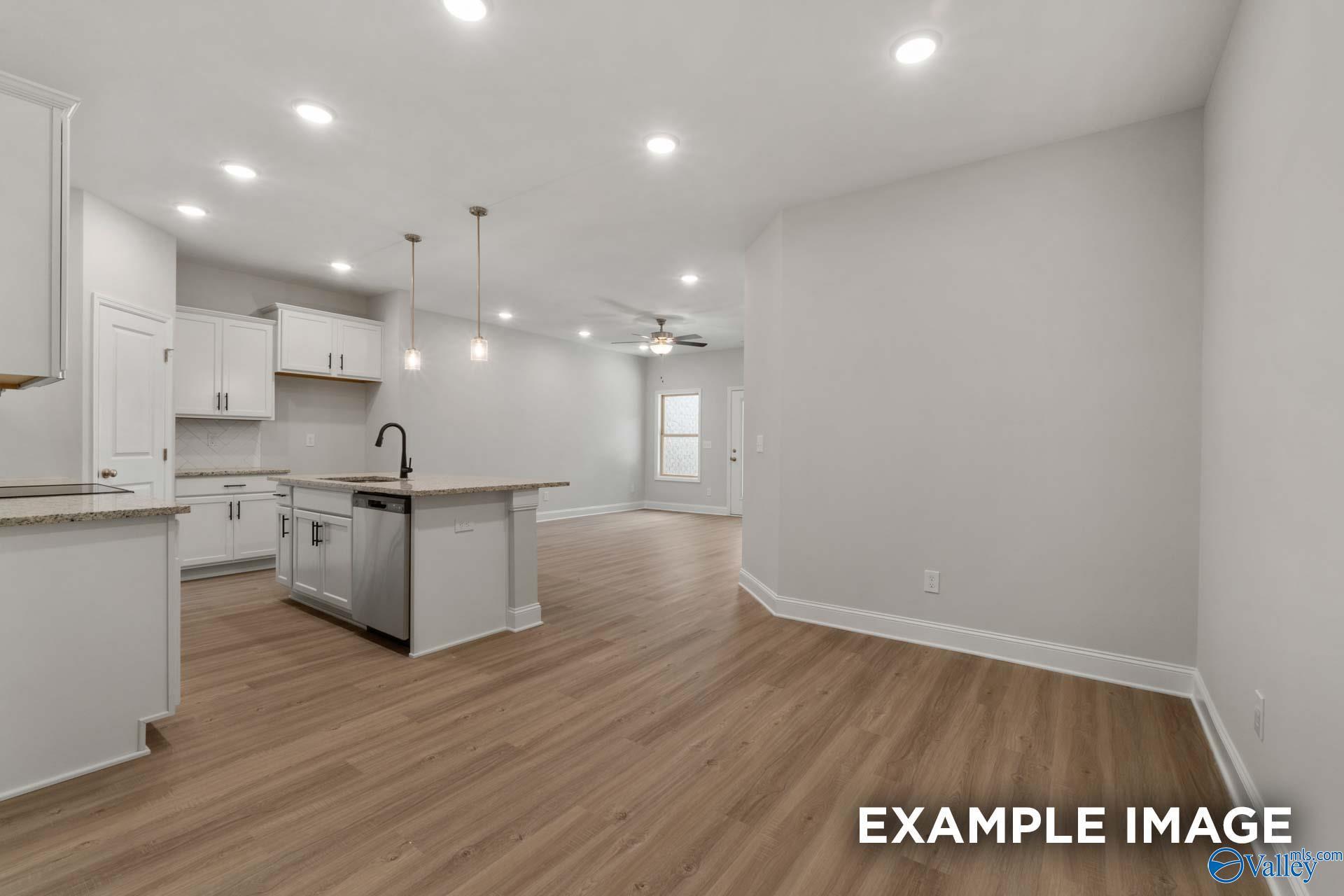 Modern kitchen featuring white cabinets, granite island sink, and hardwood floors in Davidson Homes The Camilla C, Hartselle, AL