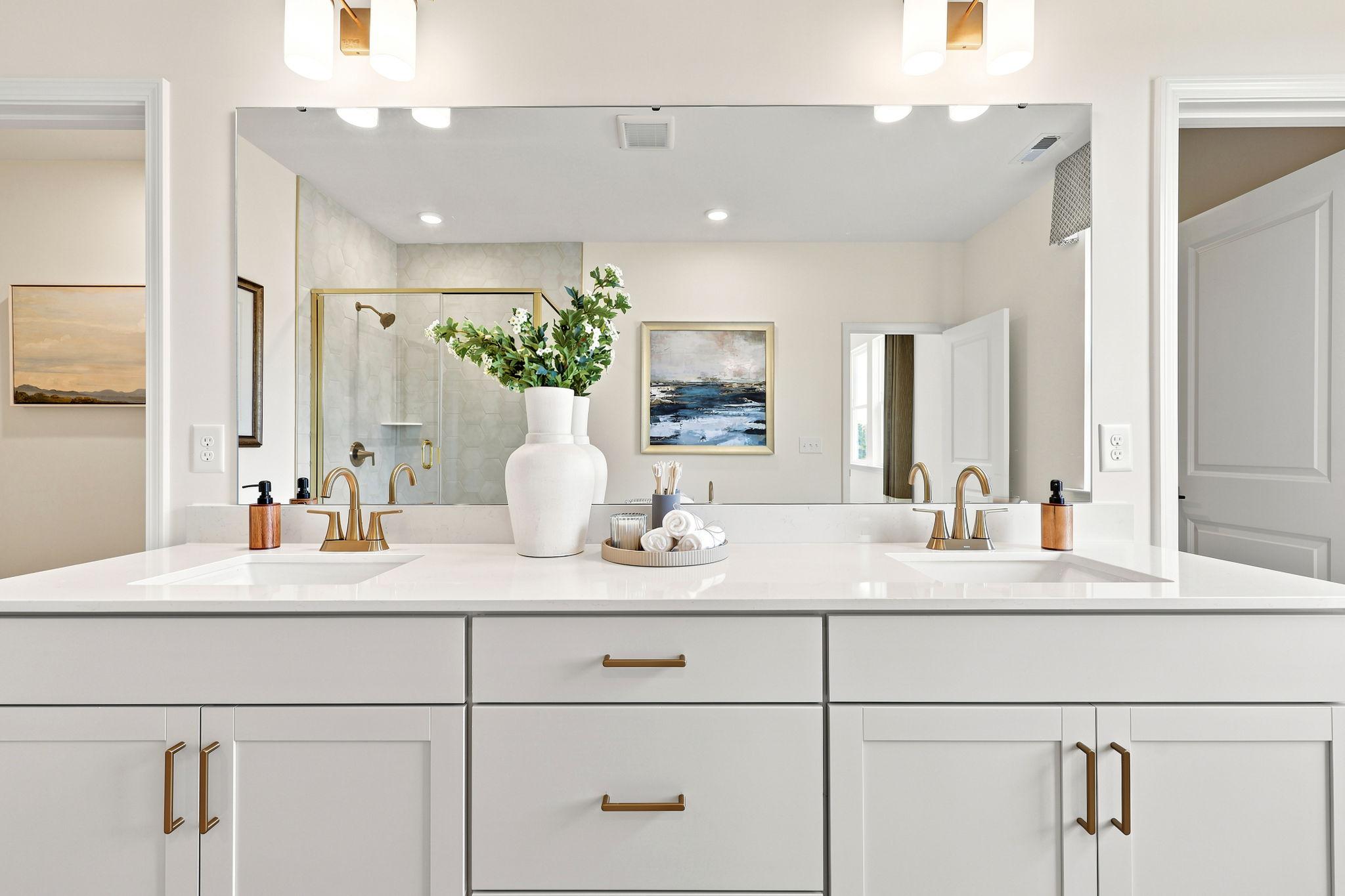 Modern master bathroom vanity in The Beech B featuring dual sinks, white cabinetry, and elegant gold hardware.