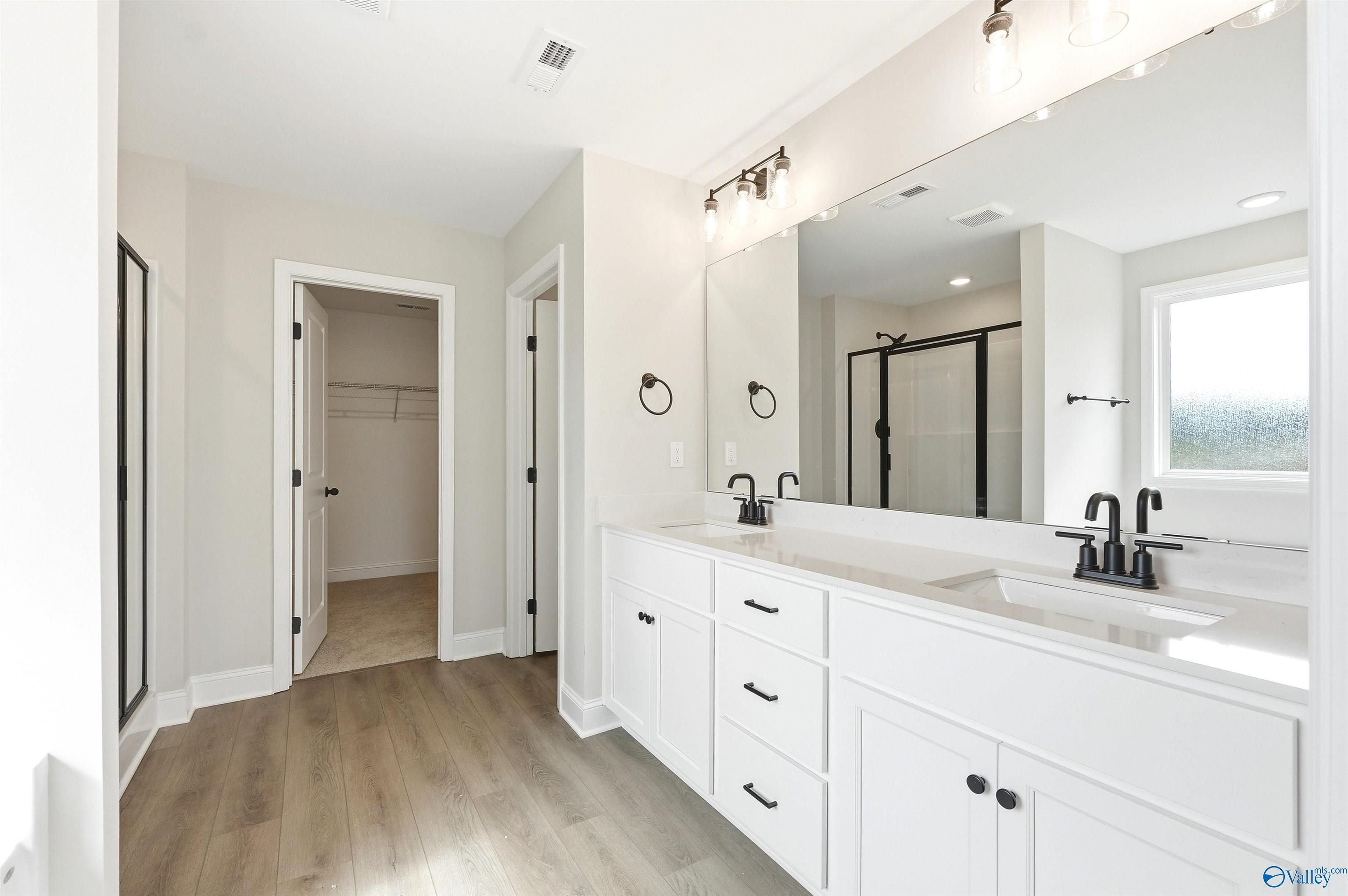 Modern primary bathroom with double vanity, matte black fixtures, and walk-in closet in The Chelsea D, Berry Cove, Alabama.
