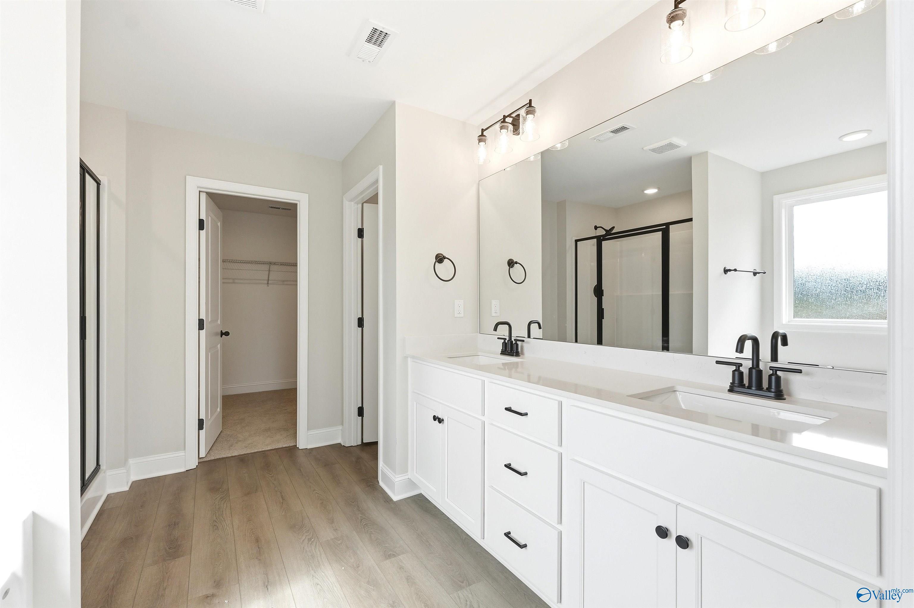 Modern primary bathroom with double vanity, matte black fixtures, and walk-in closet in The Chelsea D, Berry Cove, Alabama.