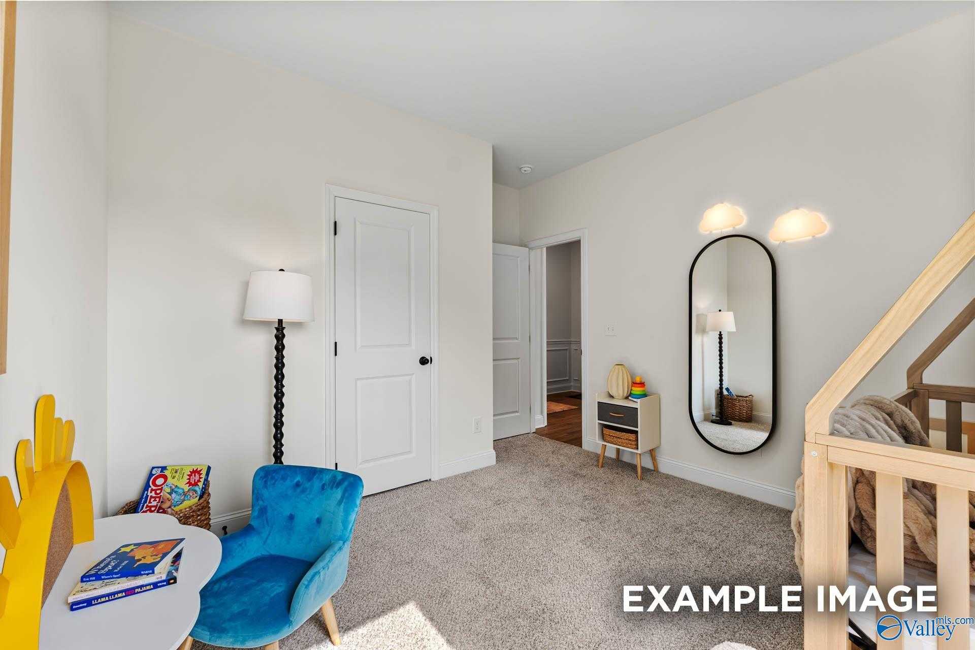 Cozy nursery featuring wooden crib, blue armchair, books, and oval mirror in Davidson Homes The Franklin, Huntsville, AL