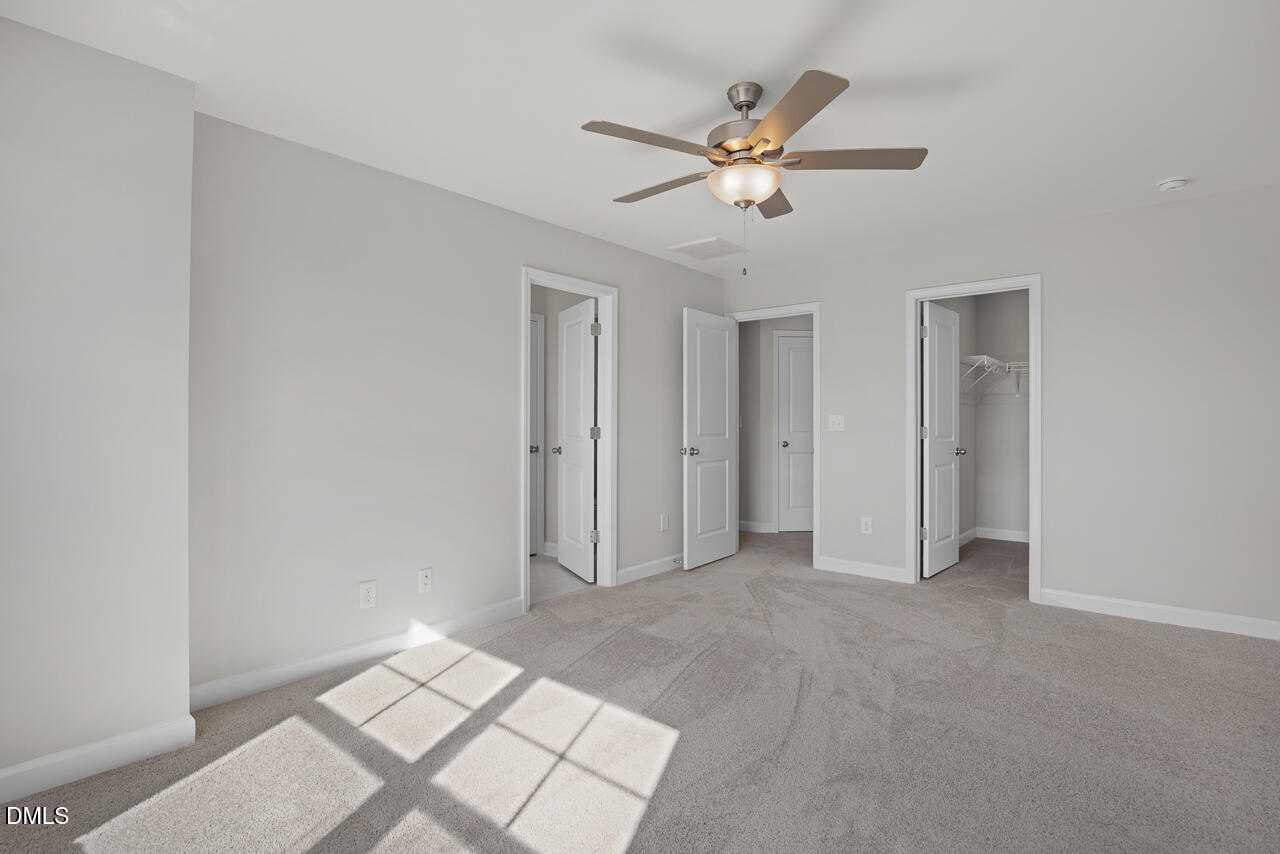 Bright upstairs bedroom with ceiling fan, walk-in closets, and sunlit windows in Davidson Homes The Warren, Fuquay-Varina, NC