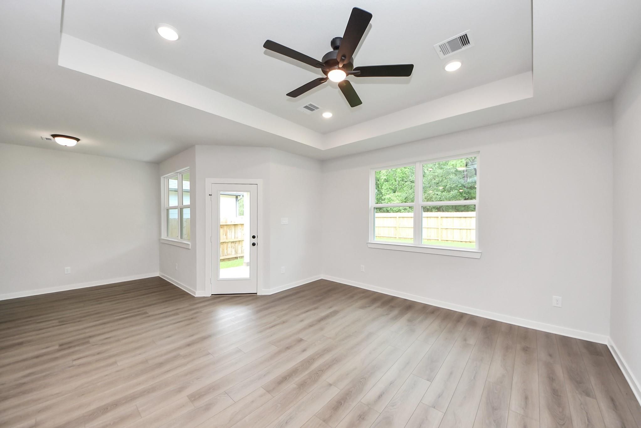 Spacious living room with tray ceiling and wood-look flooring in The Daphne F floor plan at Sundance Cove, Crosby, Texas.