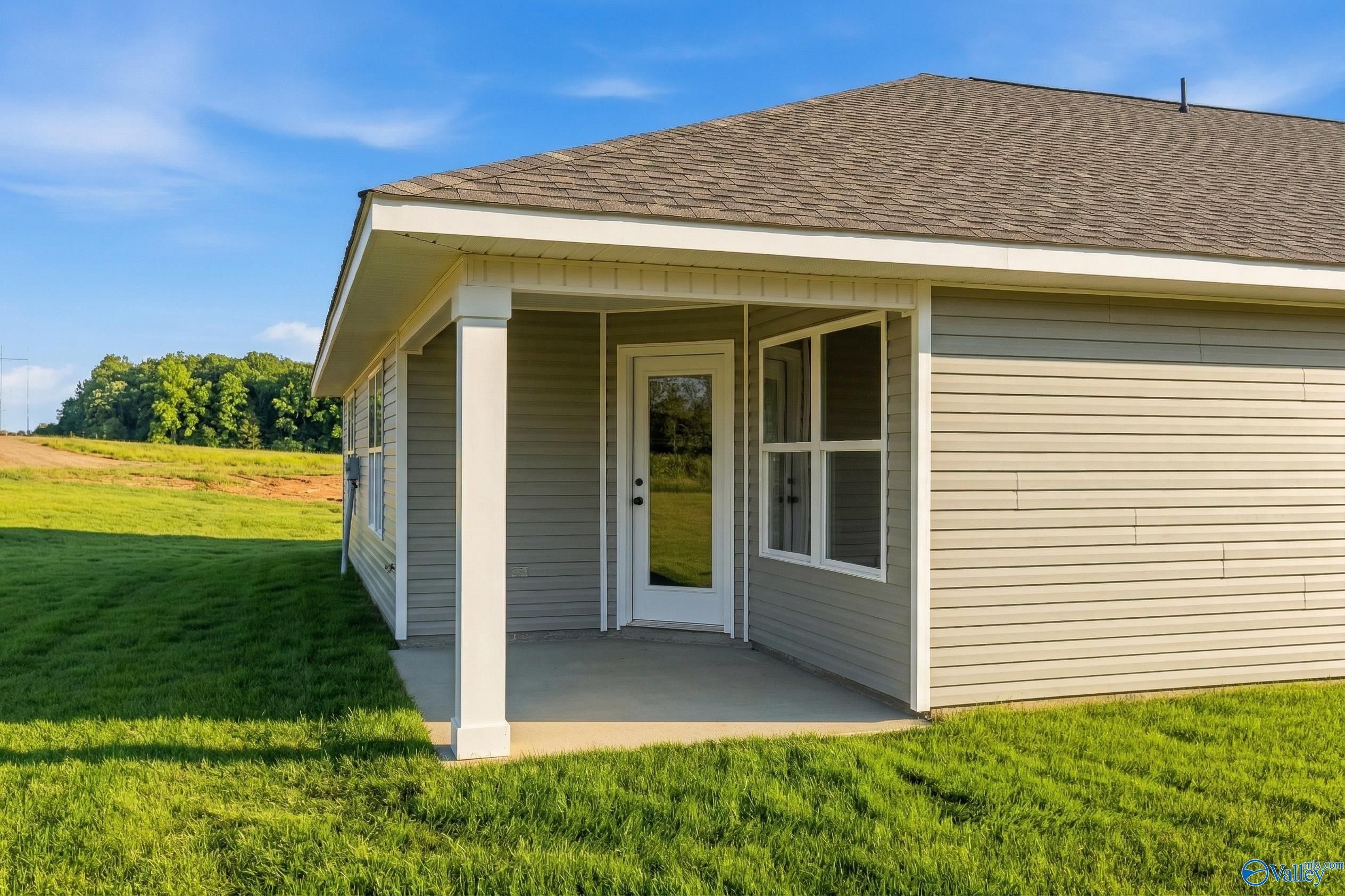 Beige single-story home with covered porch, glass entry door, and sidelight windows amid green lawn and fields in Chapel Hill, Athens, Alabama - Davidson Homes The Daphne V