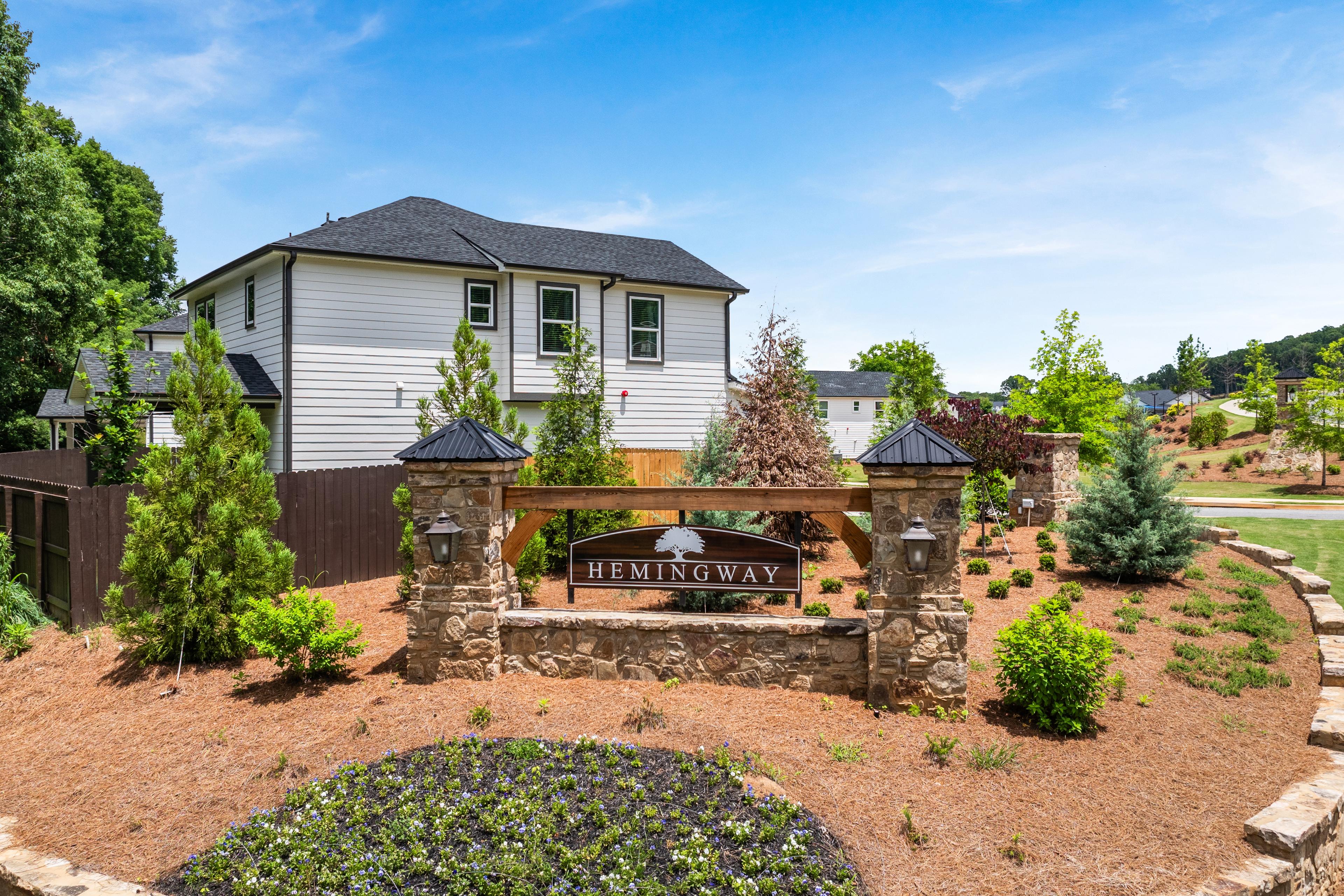 Stone entrance monument at Hemingway community in Cumming, Georgia by Davidson Homes with landscaped gardens and new houses.