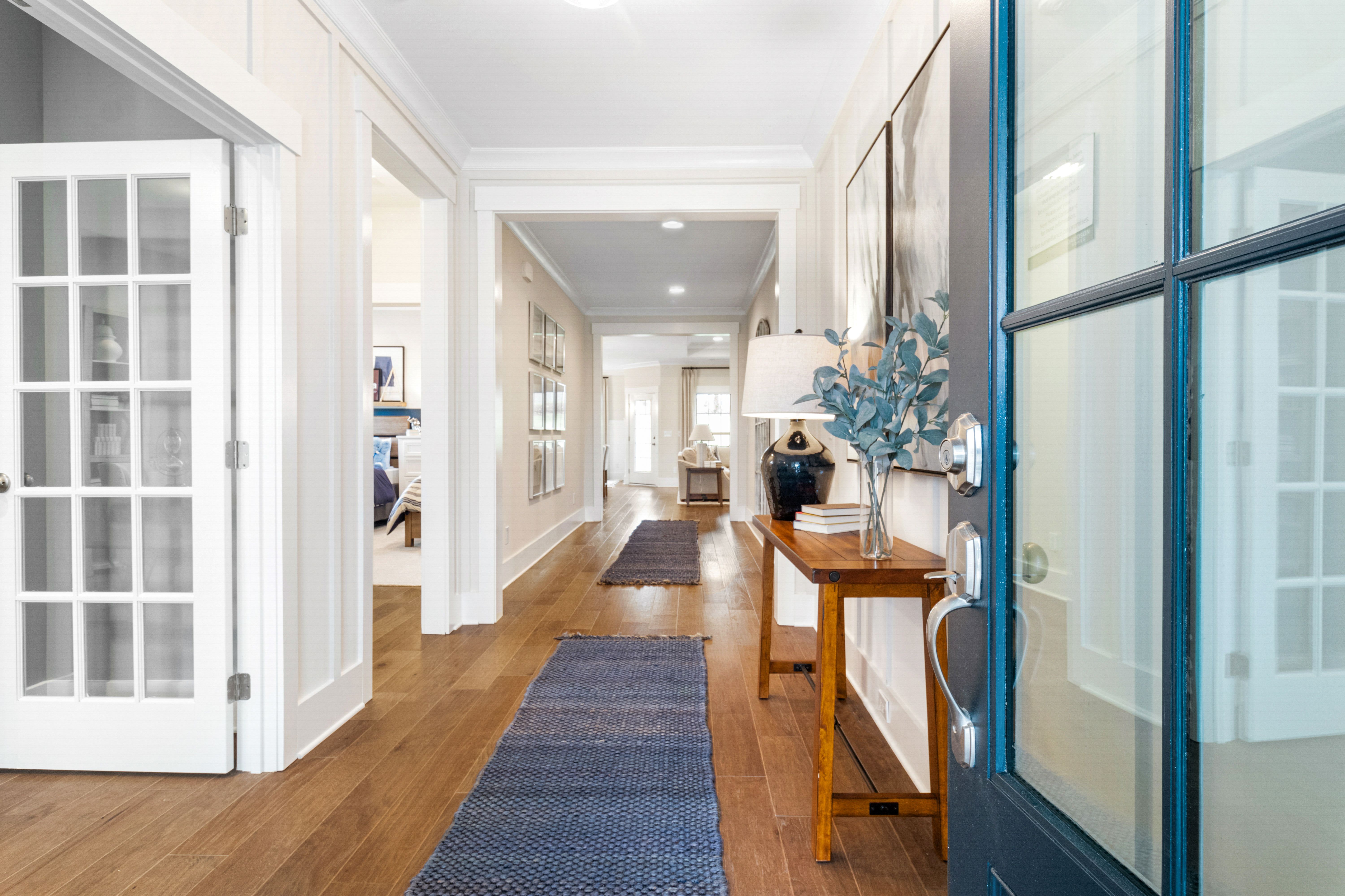 Spacious hallway in Noble Ridge Cullman Alabama home with hardwood floors, white shiplap walls, blue rug, and console table accents