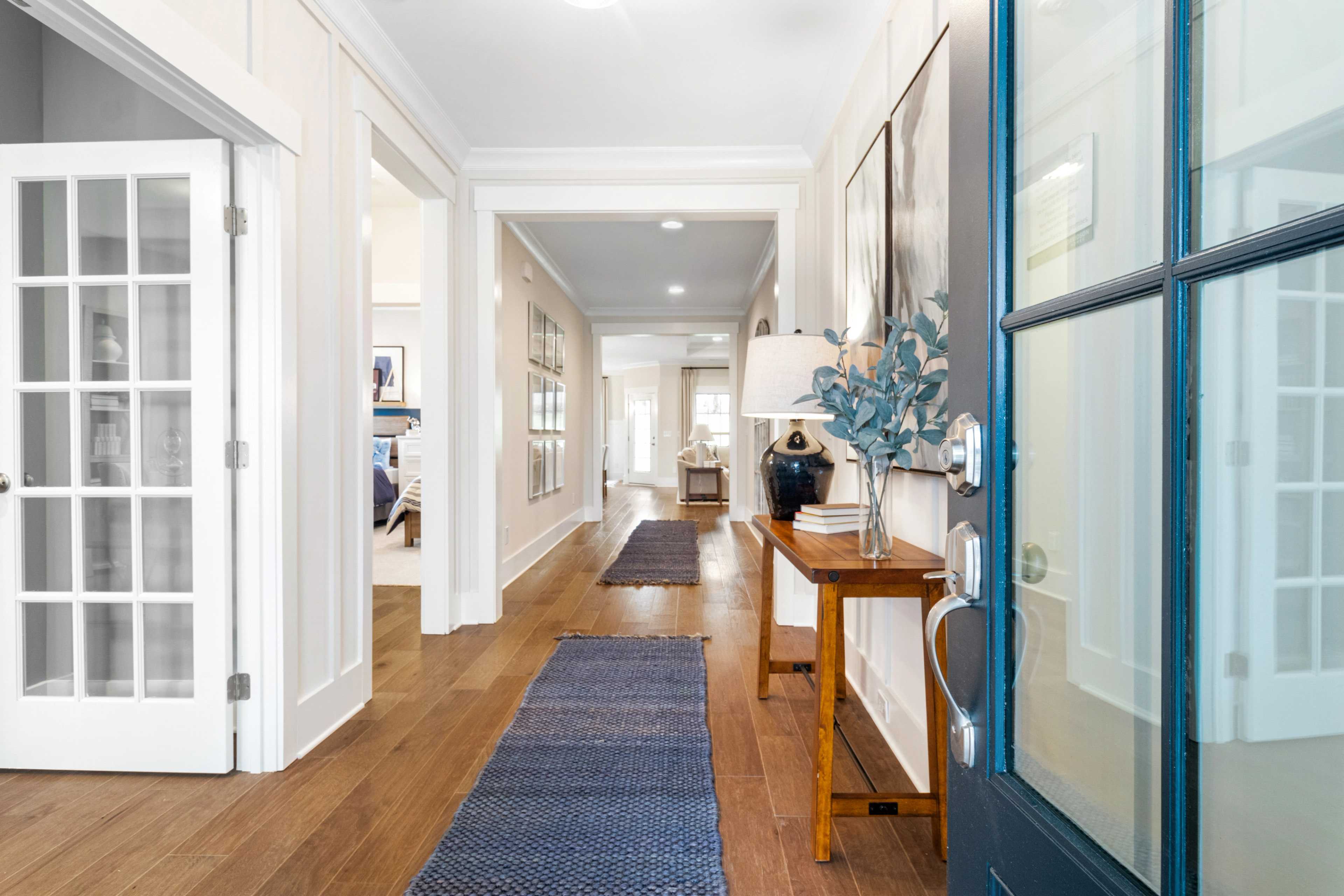 Spacious hallway in Noble Ridge Cullman Alabama home with hardwood floors, white shiplap walls, blue rug, and console table accents
