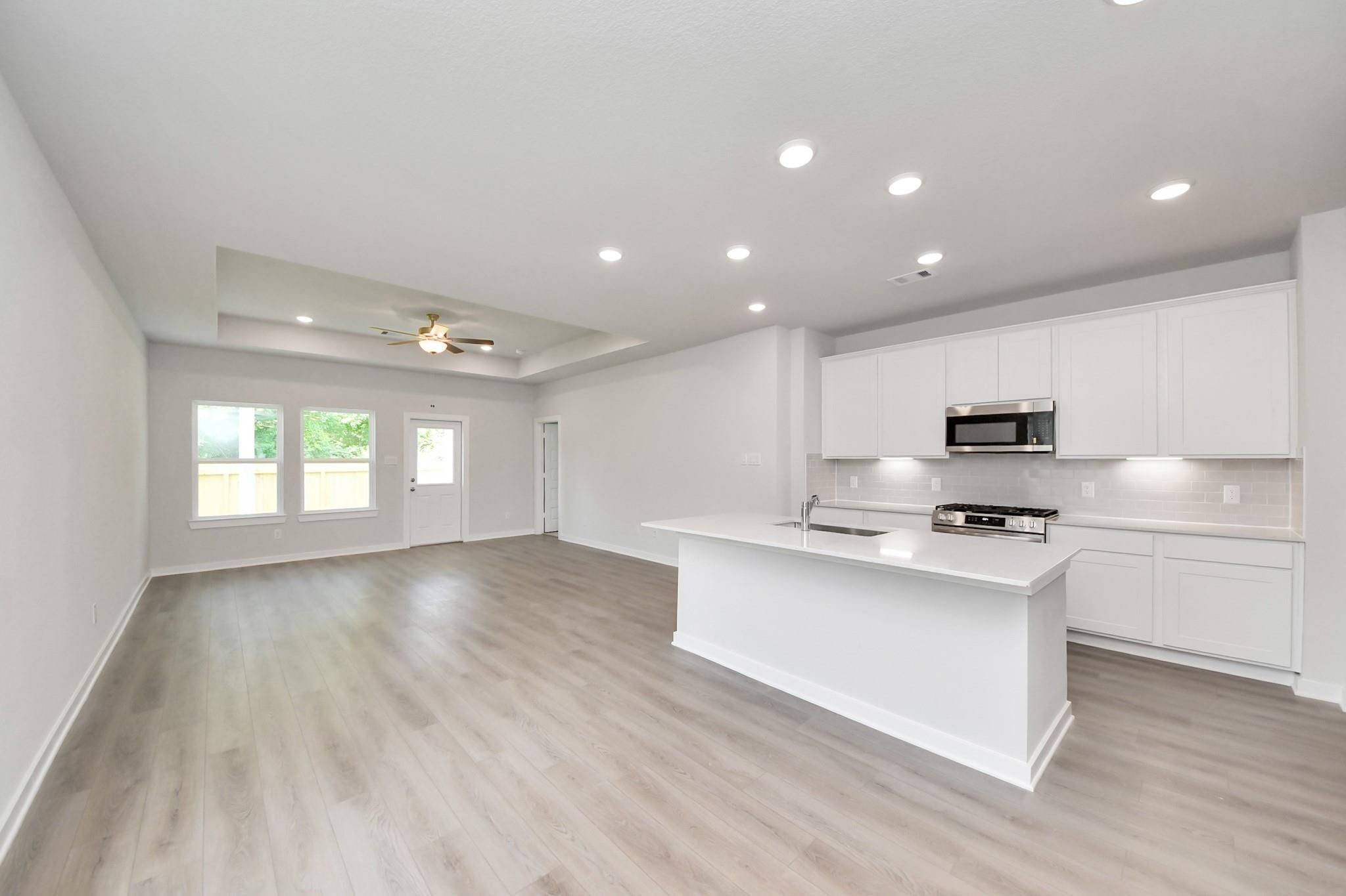 Open-concept kitchen with white cabinets and island in The Blanco E floor plan at Caney Creek Place, Conroe, Texas.