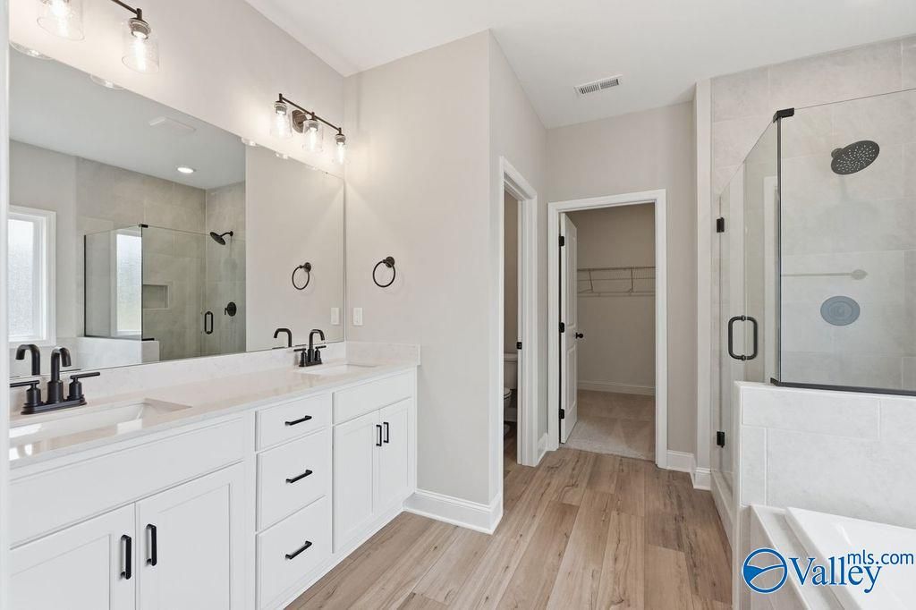 Modern master bathroom with dual vanity, glass-enclosed shower, and walk-in closet in The Rockford plan, Cain Park, Hartselle.
