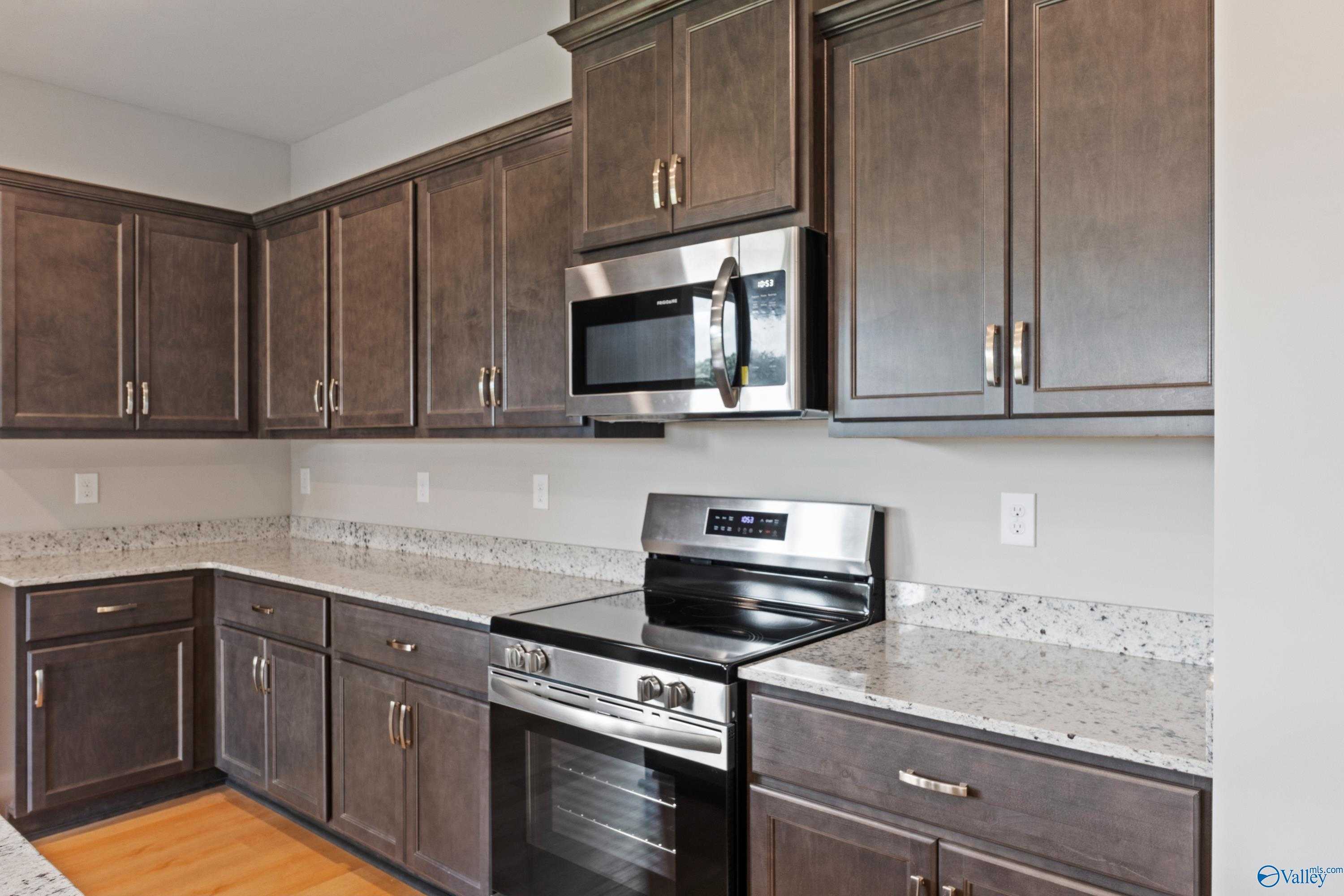 Modern shaker-style kitchen with stainless steel appliances and granite countertops in Evermore Homes The Aurora, Harvest, Alabama