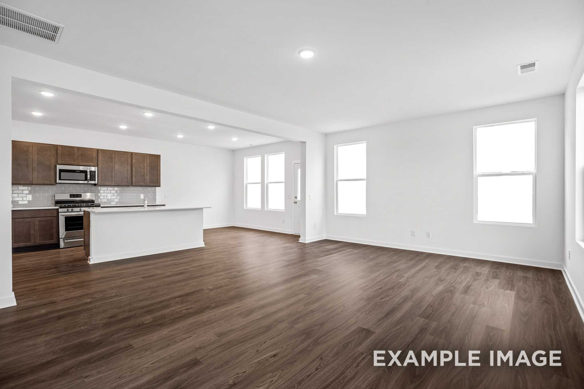 Spacious open-concept kitchen in The Grayson C with brown shaker cabinets, white quartz island, stainless appliances, and hardwood floors