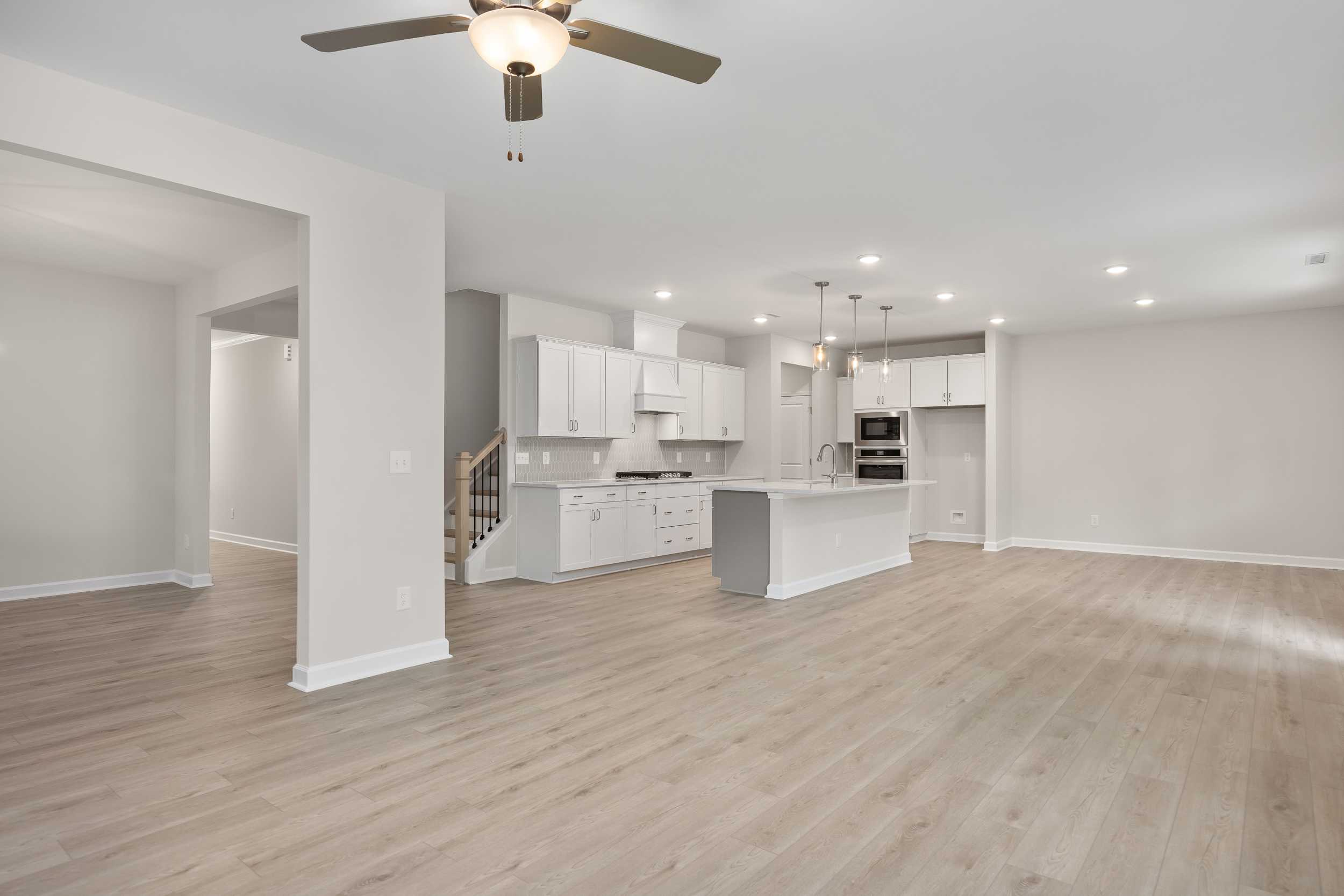 Spacious open kitchen in The Beech C with white cabinetry, large island sink, pendant lights, and hardwood floors