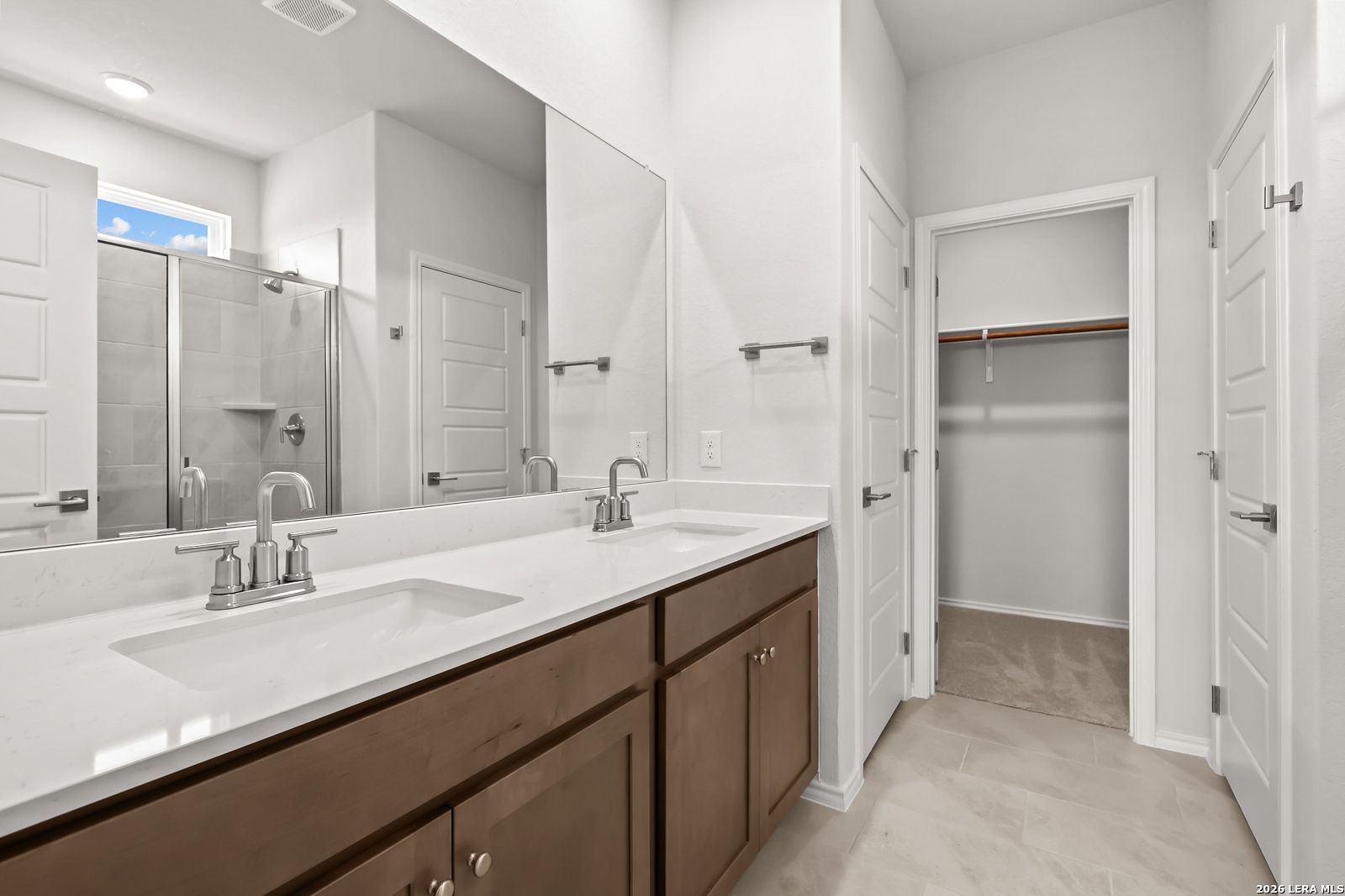 Dual vanity bathroom with white quartz countertop, walk-in shower, and walk-in closet in Davidson Homes The Daphne I, San Antonio
