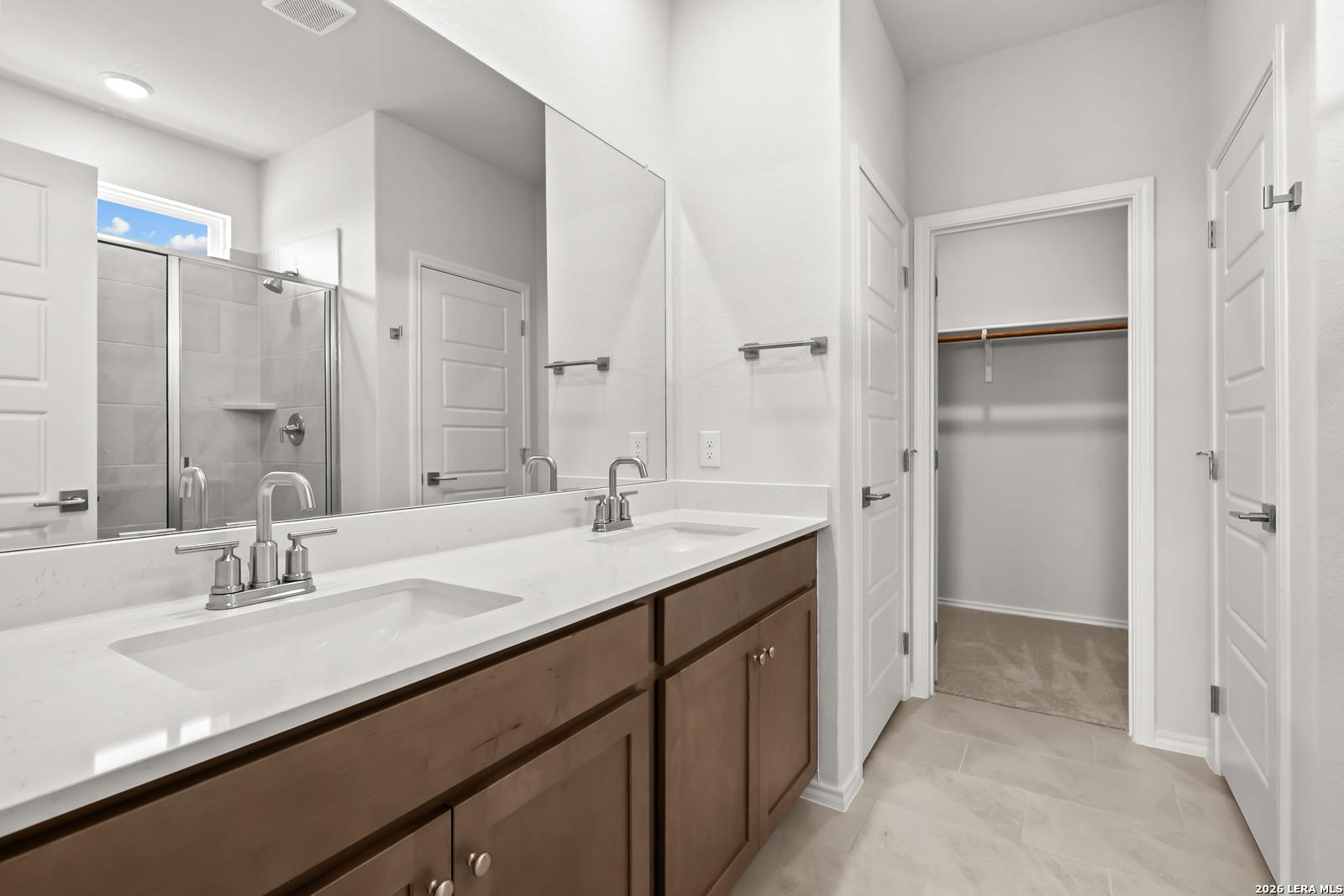 Dual vanity bathroom with white quartz countertop, walk-in shower, and walk-in closet in Davidson Homes The Daphne I, San Antonio