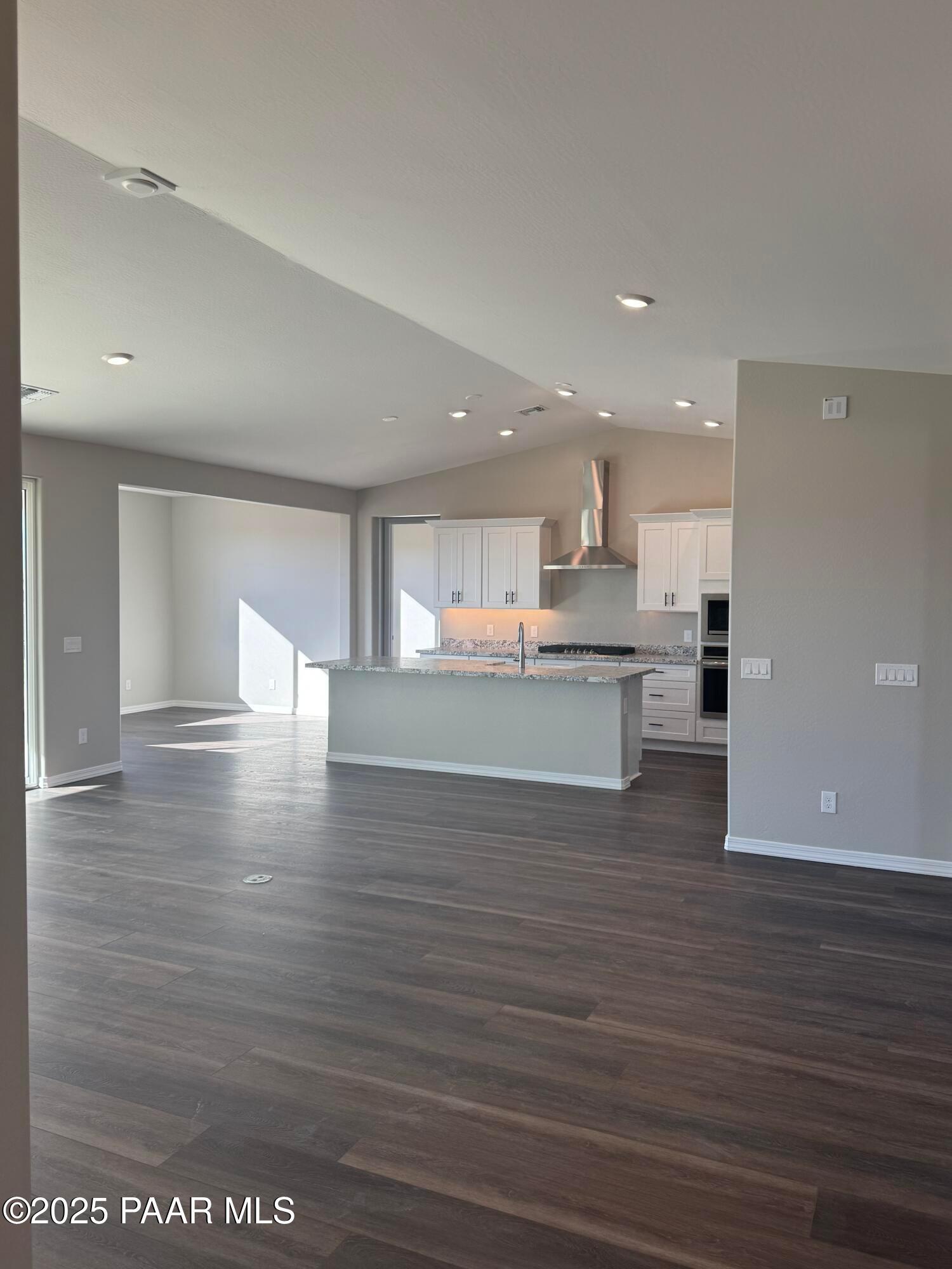 Open-concept kitchen with white cabinets, large center island, stainless cooktop, and hardwood floors in Davidson Homes The Monarch E, Prescott AZ
