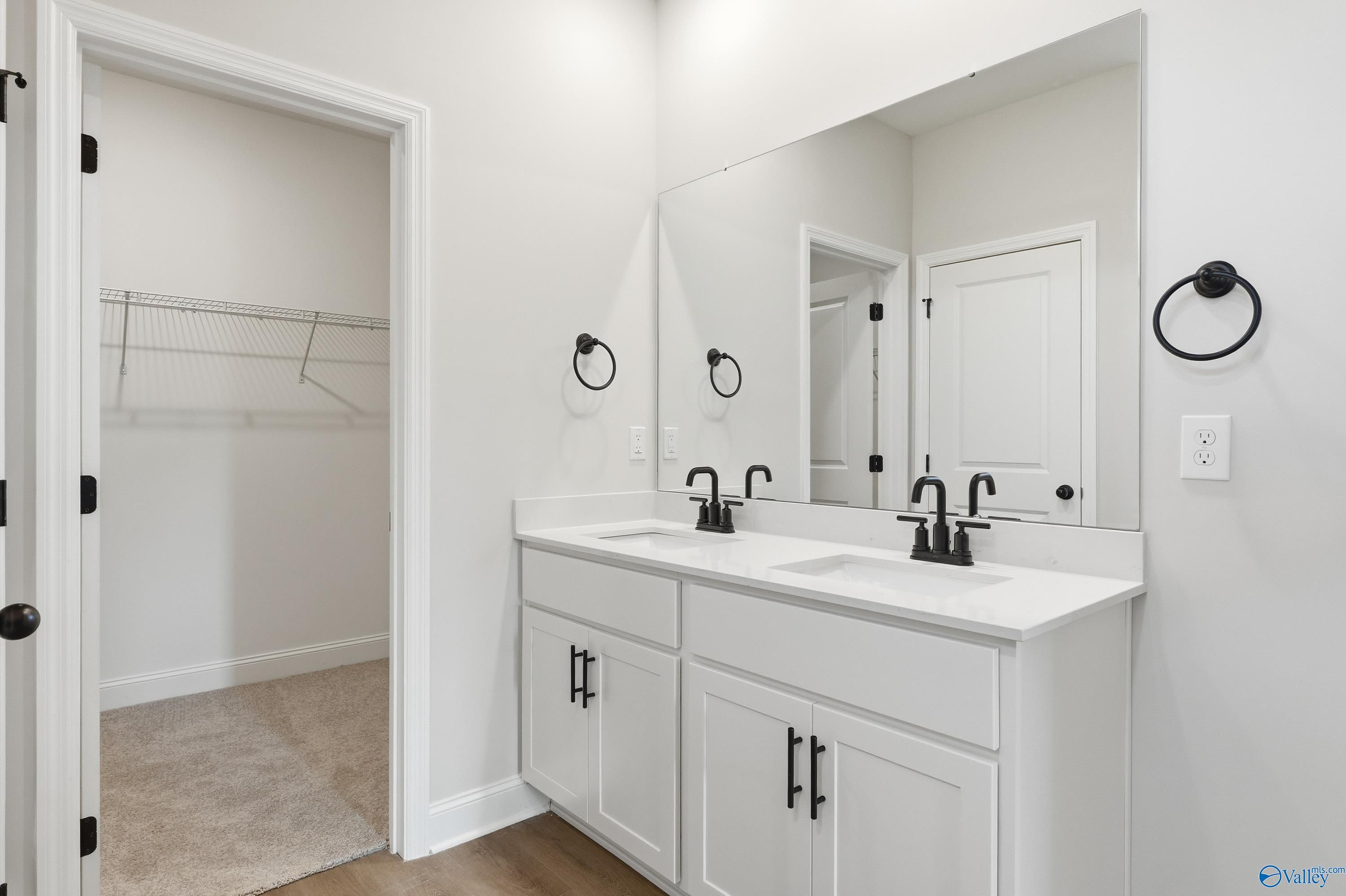 Modern master bathroom featuring double vanity sinks, large mirror, and adjacent walk-in closet in Davidson Homes The Franklin E, Hazel Green, Alabama