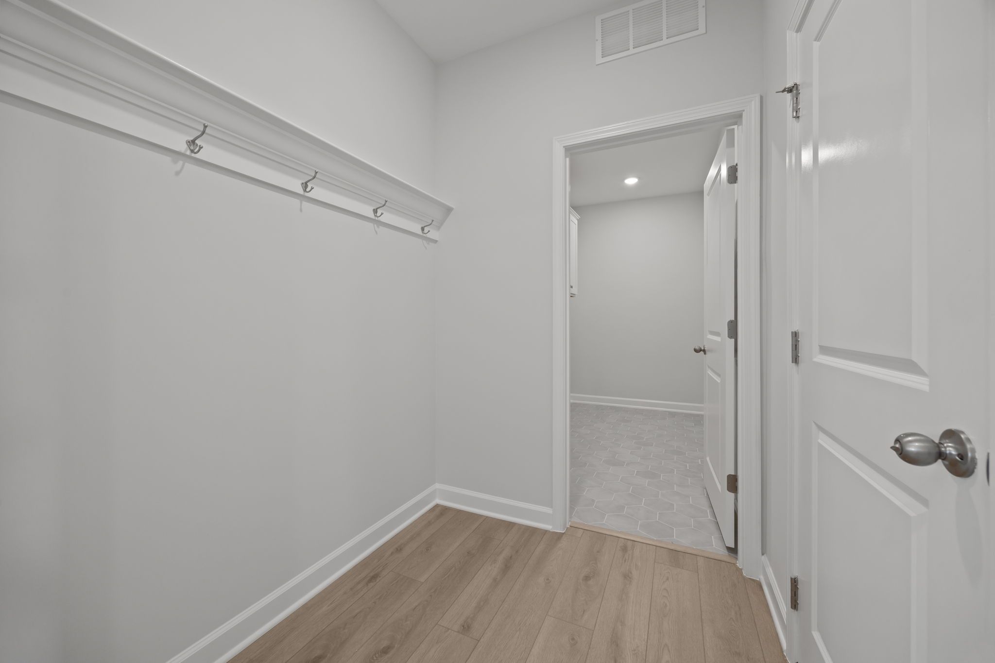Mudroom entry in The Ashport featuring wall hooks, wood-look flooring, and a doorway leading to a tiled laundry room.