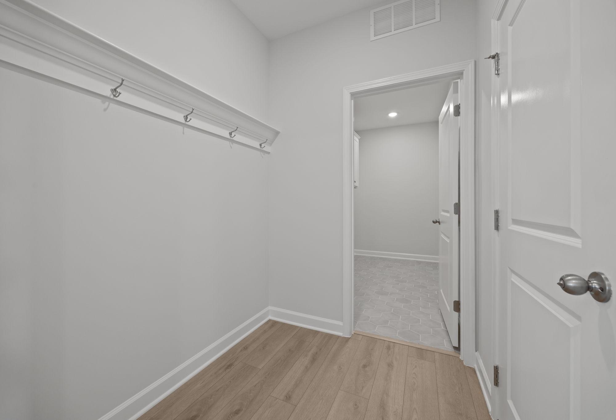 Mudroom entry in The Ashport featuring wall hooks, wood-look flooring, and a doorway leading to a tiled laundry room.
