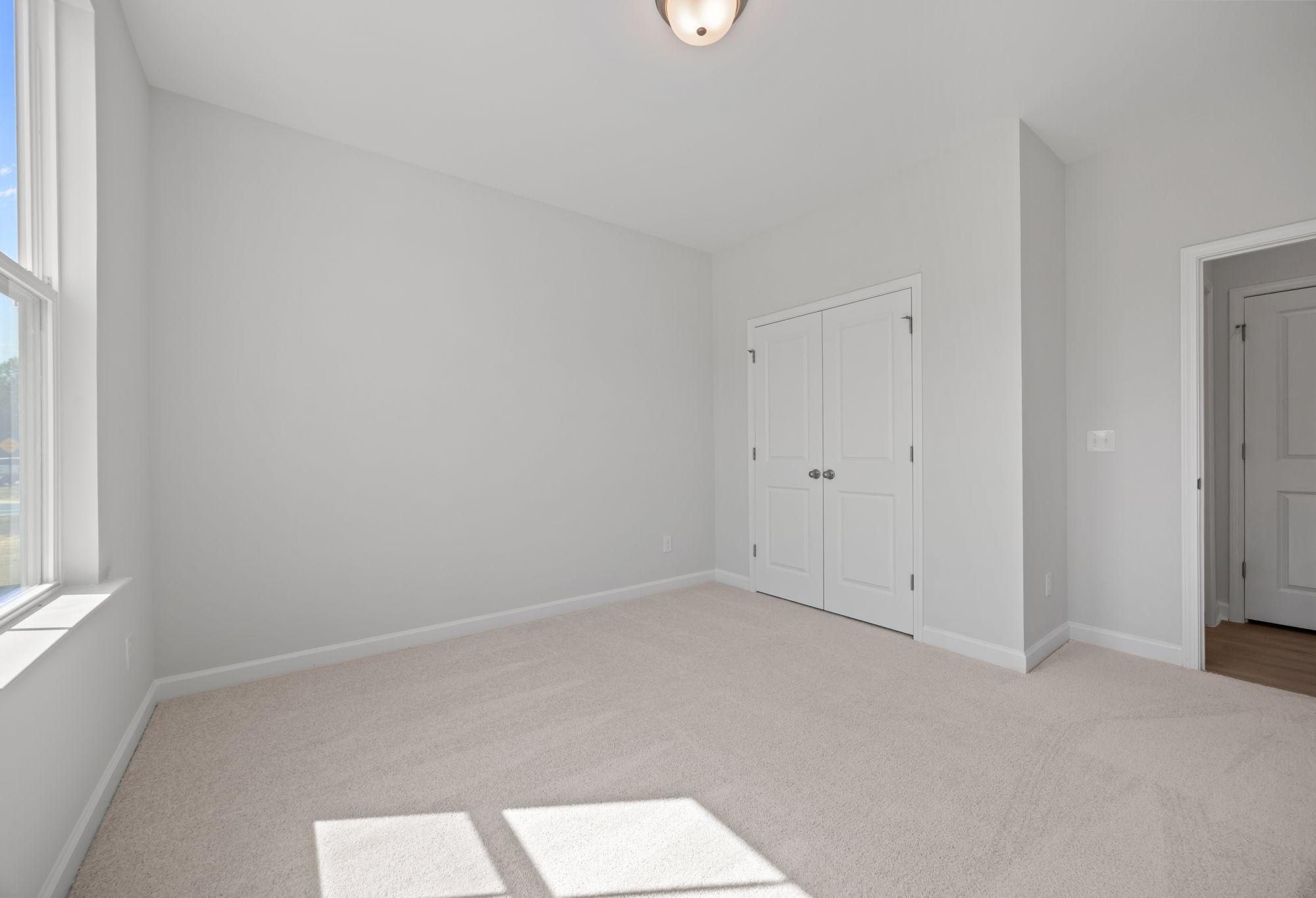 Spacious secondary bedroom in The Ashport C floor plan featuring neutral carpet, white walls, and a walk-in closet.