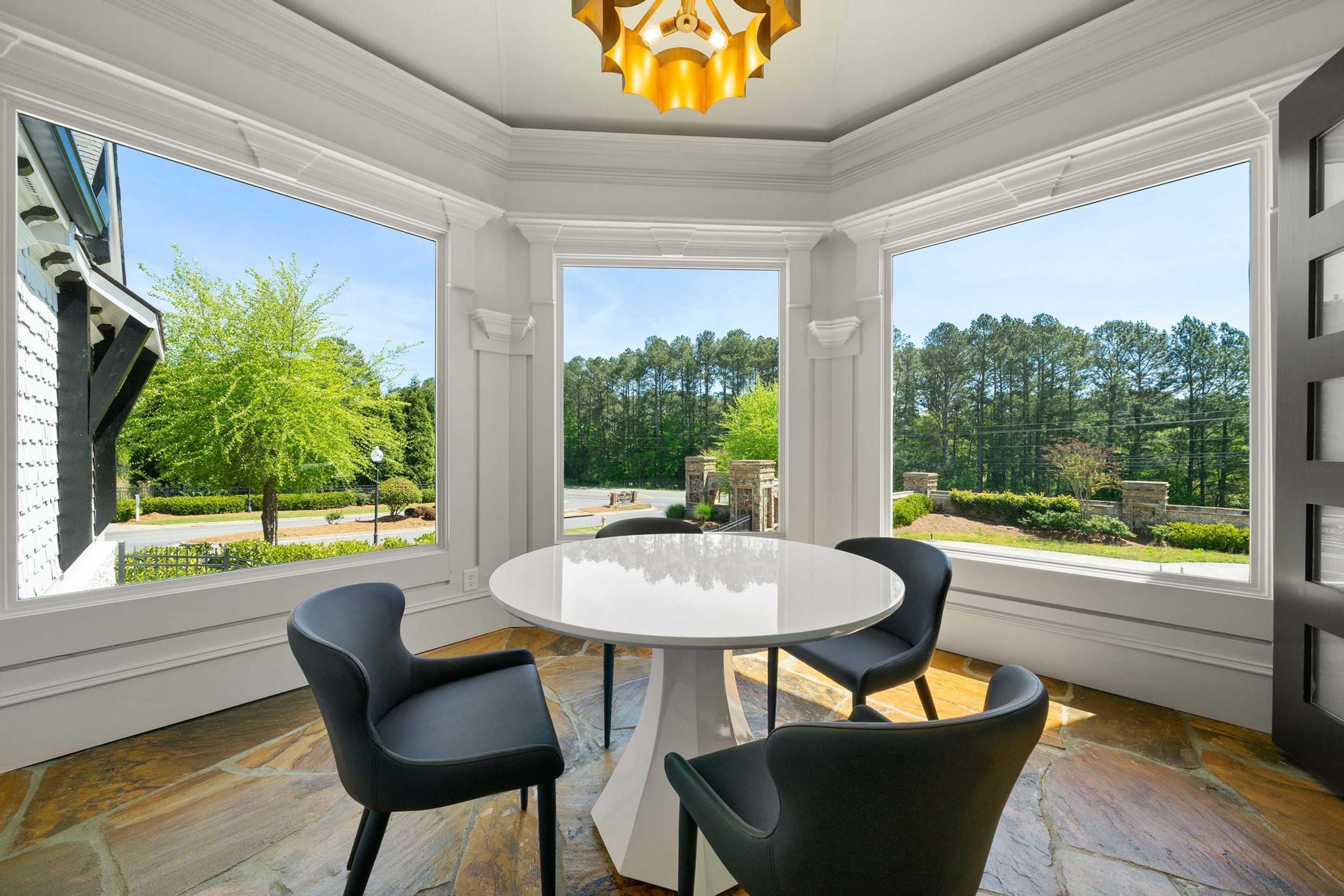 Bright sunroom at Mountainbrook in Cartersville GA with round white table, black chairs, gold chandelier, and wooded views through bay windows