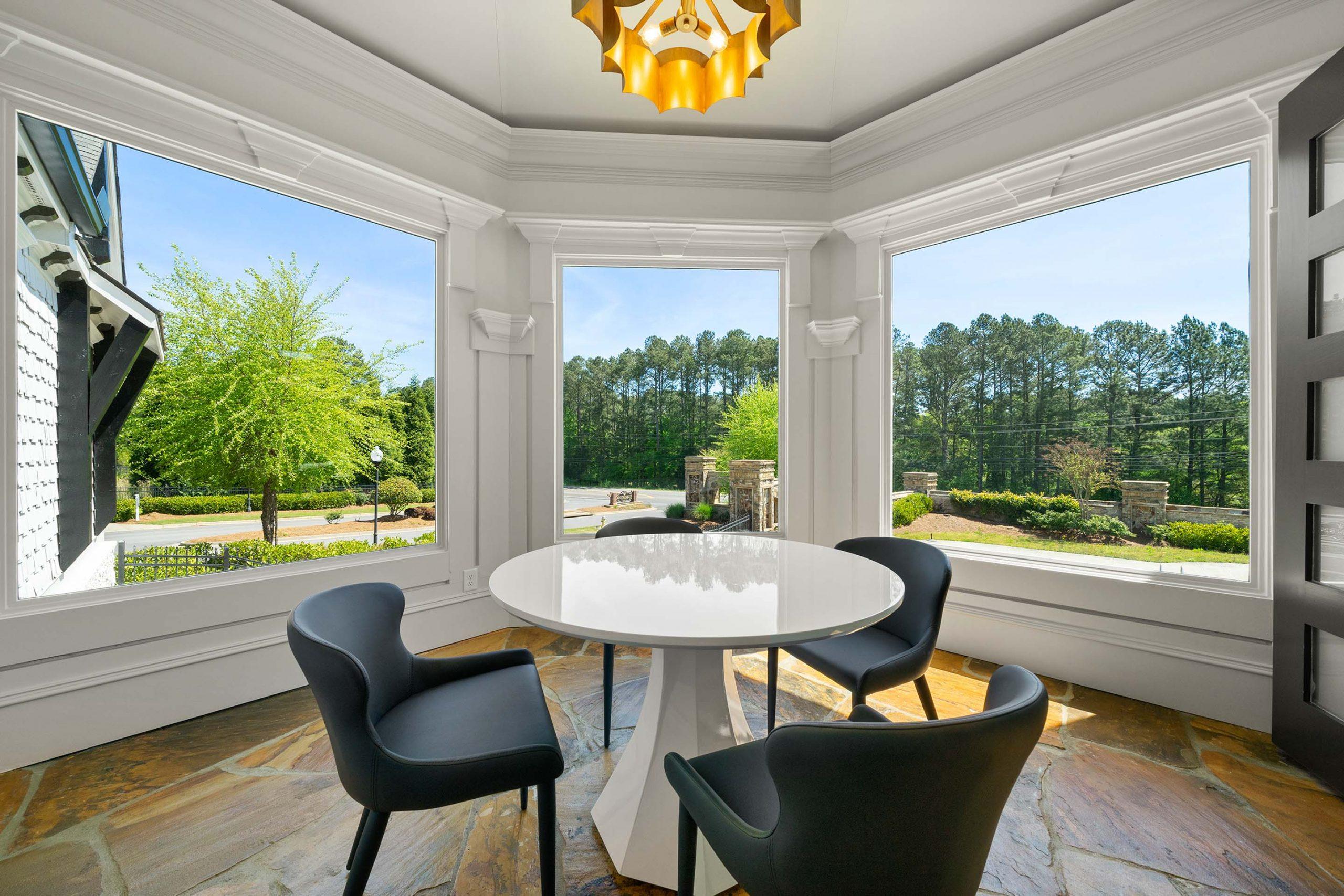 Bright sunroom at Mountainbrook in Cartersville GA with round white table, black chairs, gold chandelier, and wooded views through bay windows