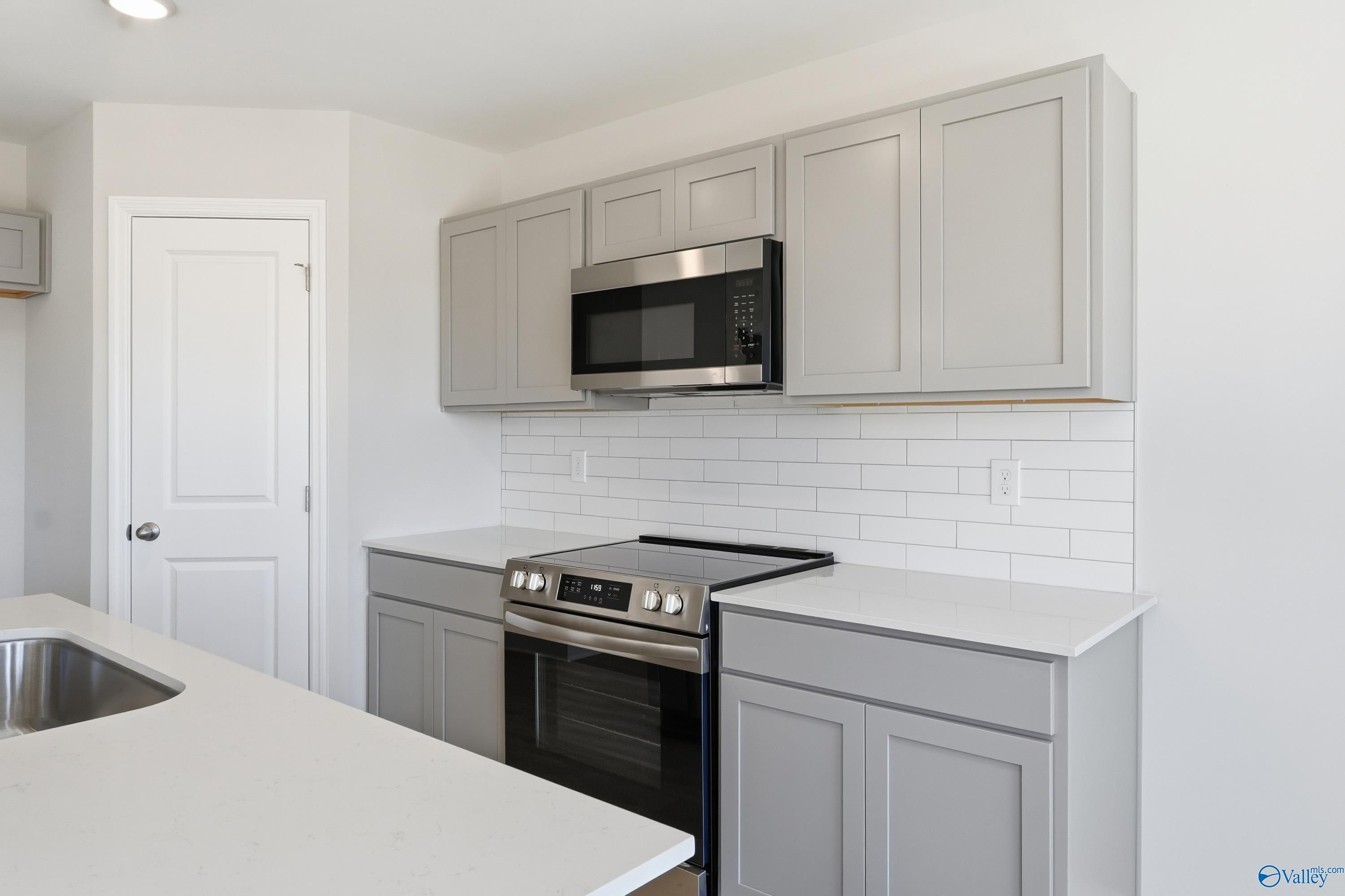 Modern kitchen with gray shaker cabinets, stainless steel appliances, white quartz counters in Davidson Homes The Butler, New Market, Alabama