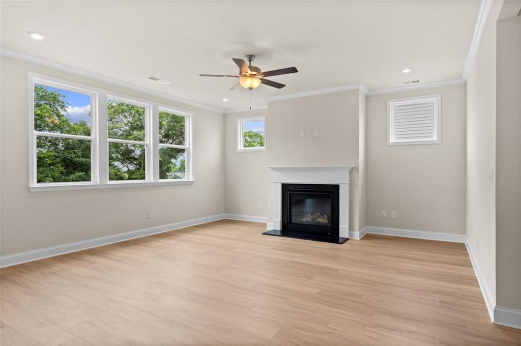 Bright living room with gas fireplace, ceiling fan, hardwood floors, and large windows overlooking trees in Davidson Homes The Hickory B, Hoschton