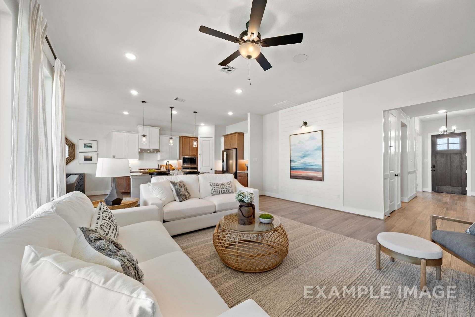 Bright open living room with white sectional sofa, rattan coffee table, and adjacent modern kitchen in Davidson Homes The Edward A, Lago Mar Texas City