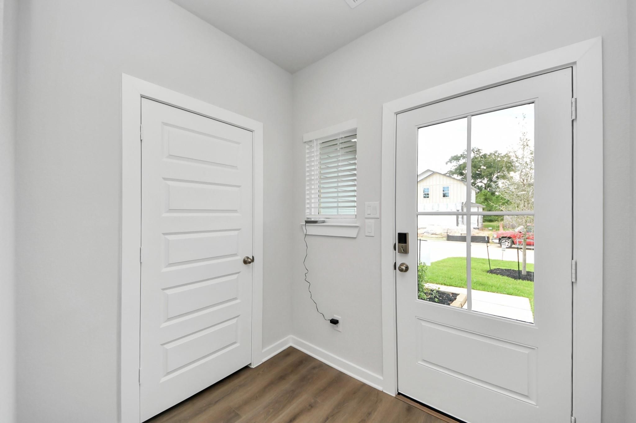 Bright white foyer entry with glass-paneled front door and wood-look flooring in Davidson Homes The Sabine F, Conroe, Texas