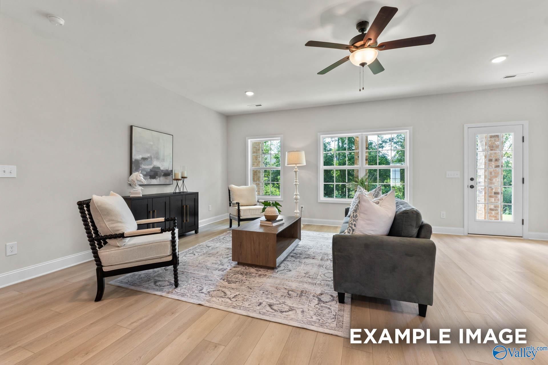 Cozy living room with gray sectional sofa, ceiling fan, large windows, and hardwood floors in Davidson Homes The Kirkland, Decatur AL