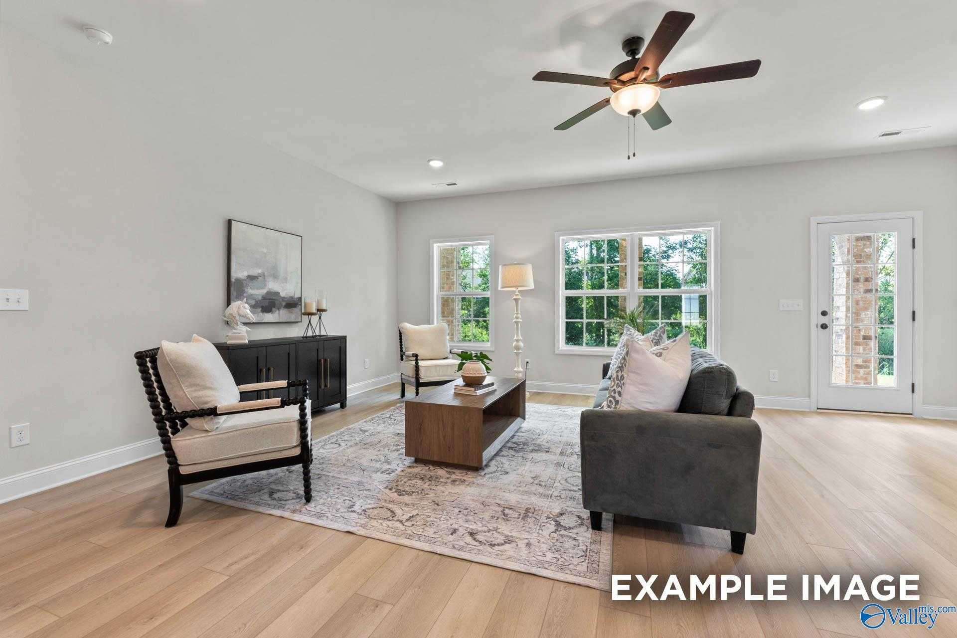 Cozy living room with gray sectional sofa, ceiling fan, large windows, and hardwood floors in Davidson Homes The Kirkland, Decatur AL