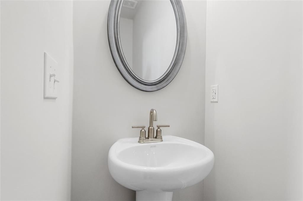 Elegant powder room featuring white pedestal sink and round mirror in Davidson Homes The Glenwood C at Wehunt Meadows, Hoschton, Georgia