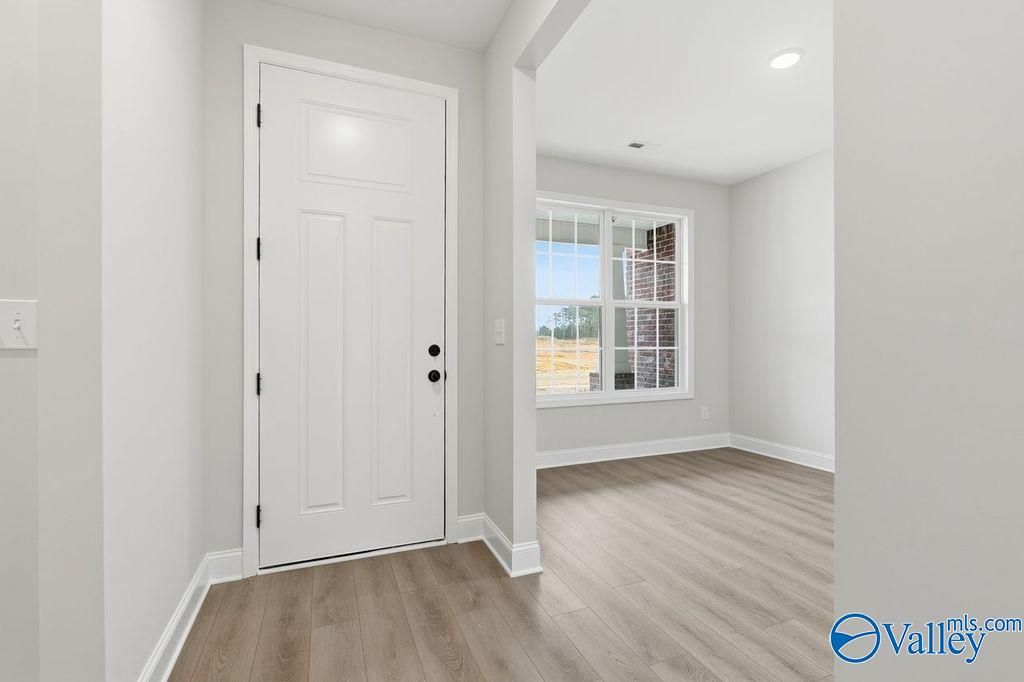 Bright entryway with open white paneled door, window overlooking yard, light wood floors in Davidson Homes The Rockford B, Hartselle, AL