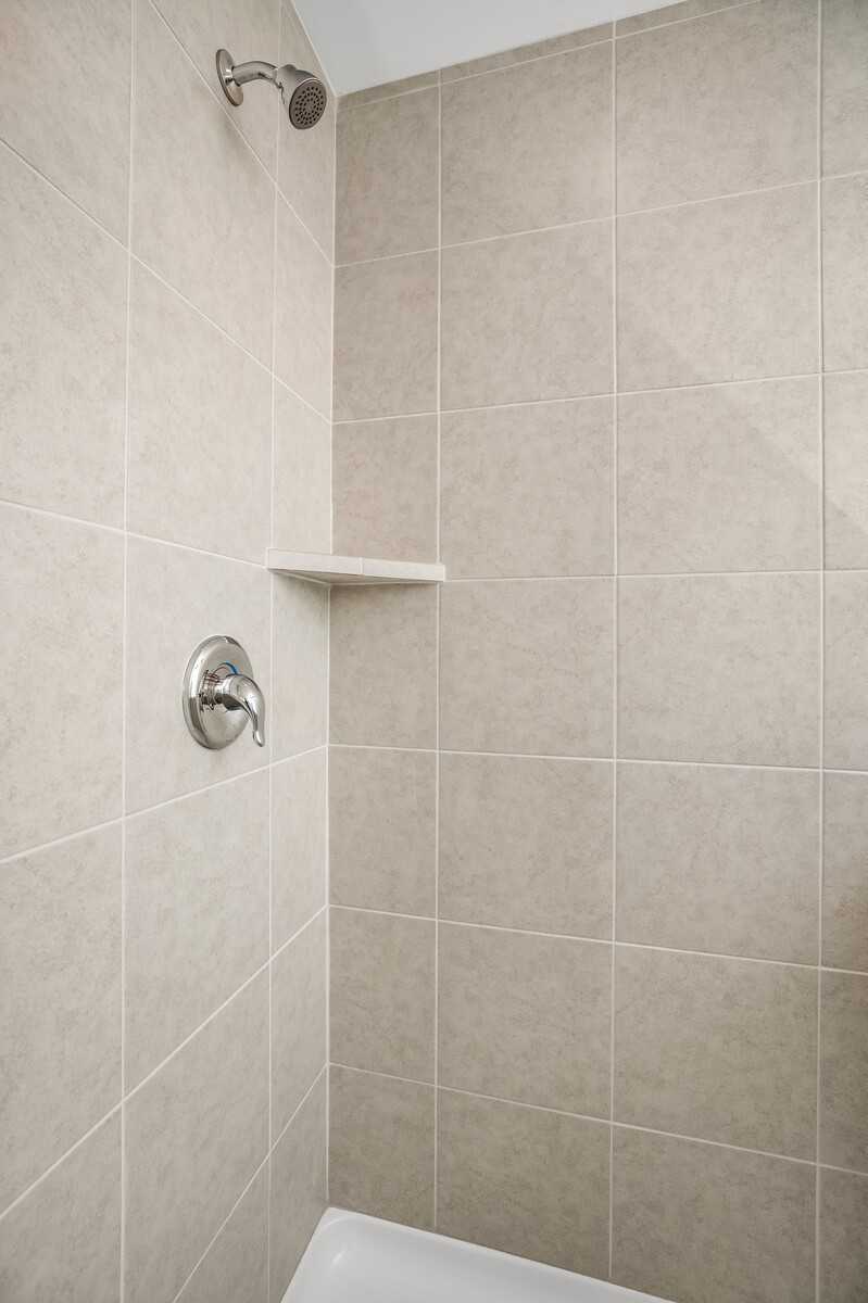Beige tiled shower enclosure with chrome fixtures and built-in shelf in Davidson Homes The Gordon B, White House, TN