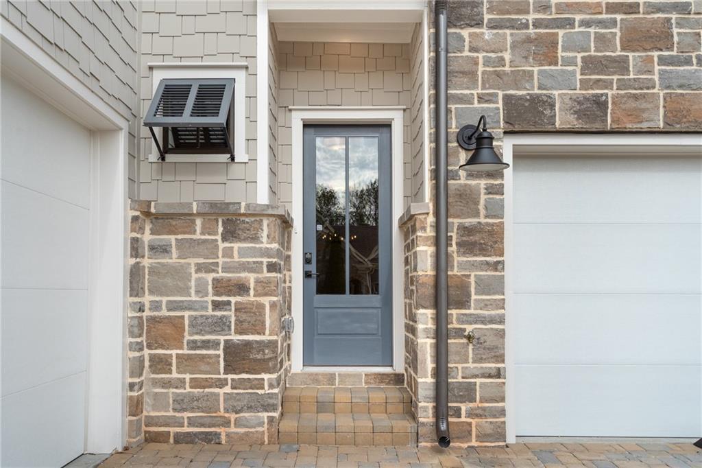 Elegant blue front door with glass panels, stone pillars, and 3-car garage in Davidson Homes The Seaside B, Woodstock, Georgia