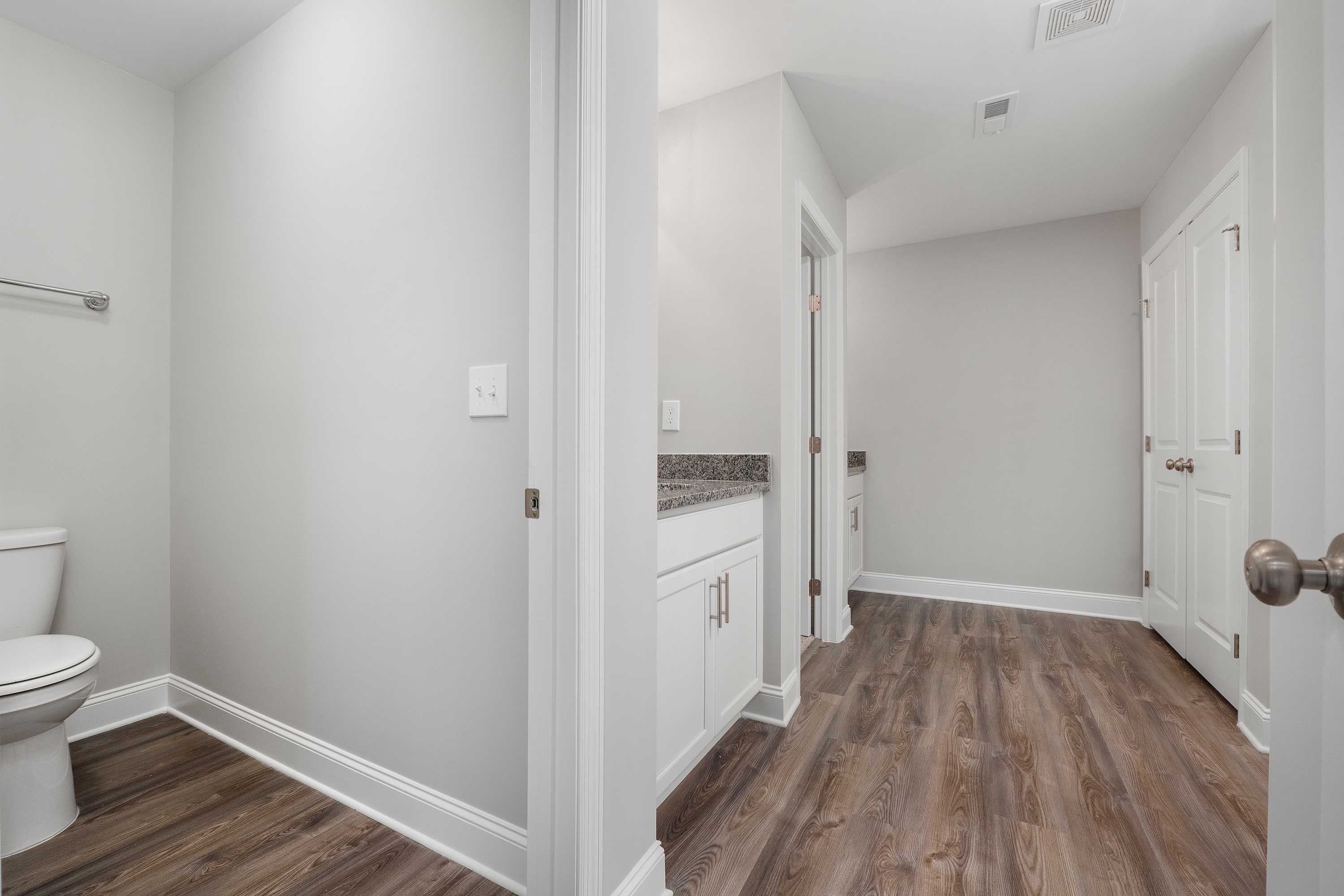 The Aiken home bathroom featuring white vanity, granite countertop, toilet, and hardwood floors in Meridianville