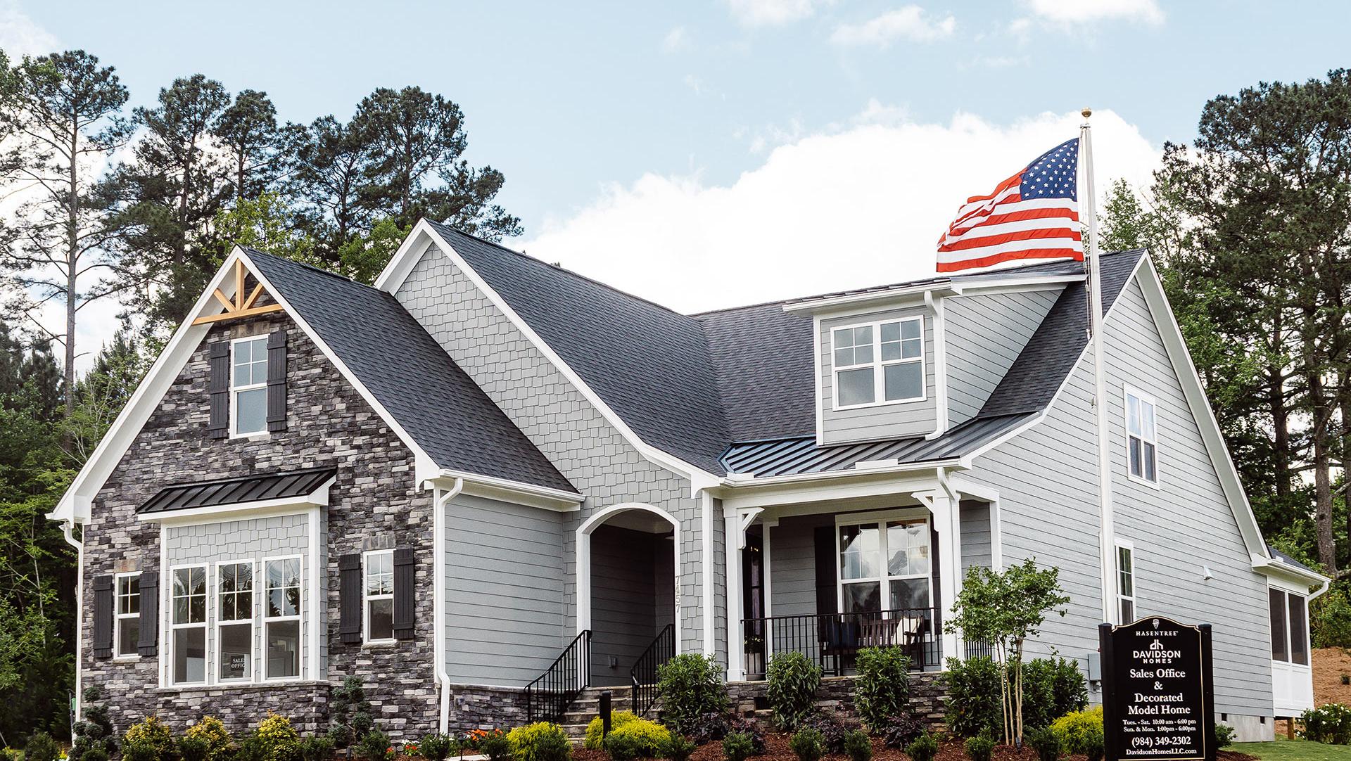 Elegant Davidson Homes residence with American flag, gray siding, stone accents, wraparound porch, and landscaped yard