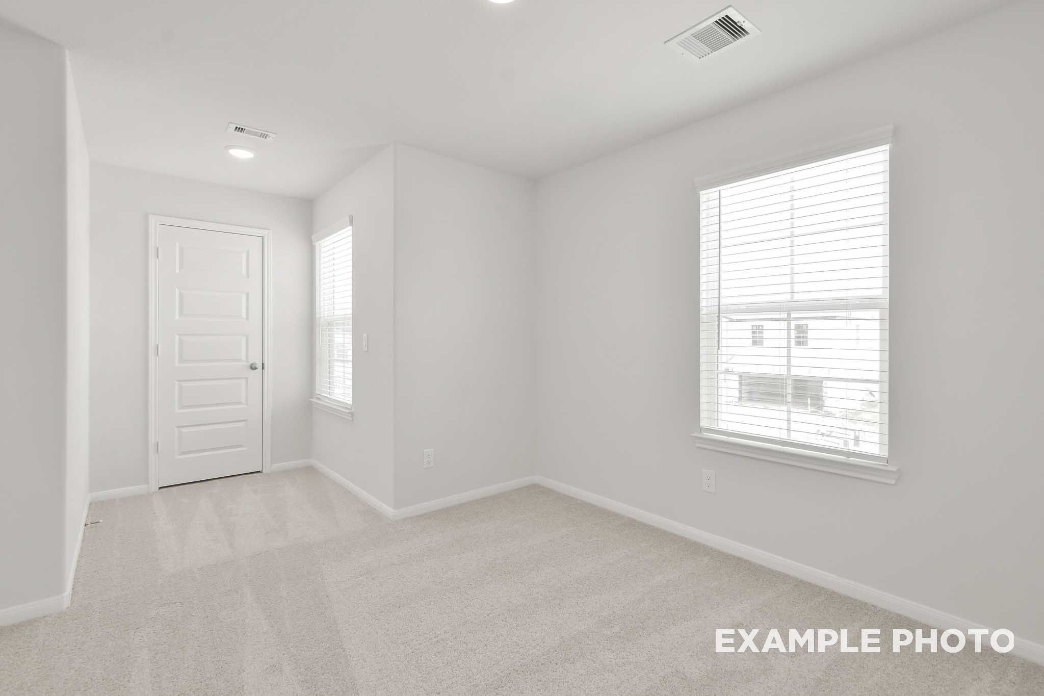 Spacious bright bedroom in The Brazos by Davidson Homes, featuring carpet flooring, white walls, and large windows with blinds
