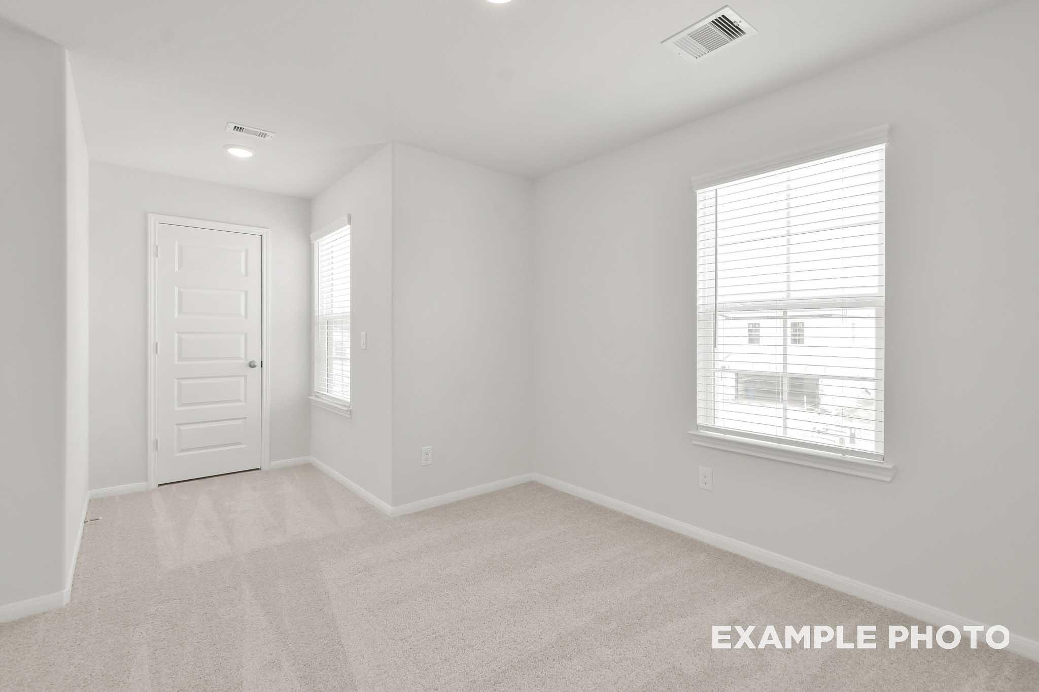 Spacious bright bedroom in The Brazos by Davidson Homes, featuring carpet flooring, white walls, and large windows with blinds