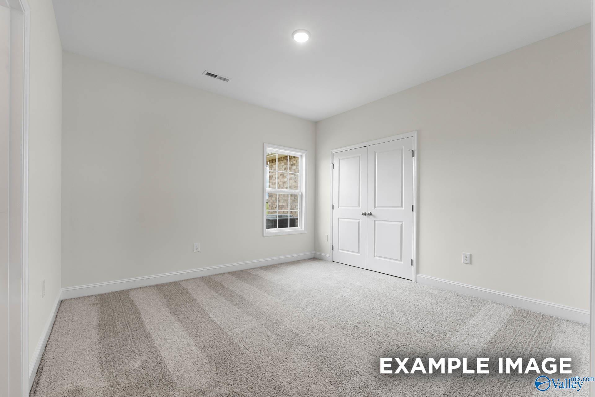 Bright secondary bedroom featuring neutral walls, patterned carpet, double closet doors, and large window in Davidson Homes The Emory, Toney, Alabama