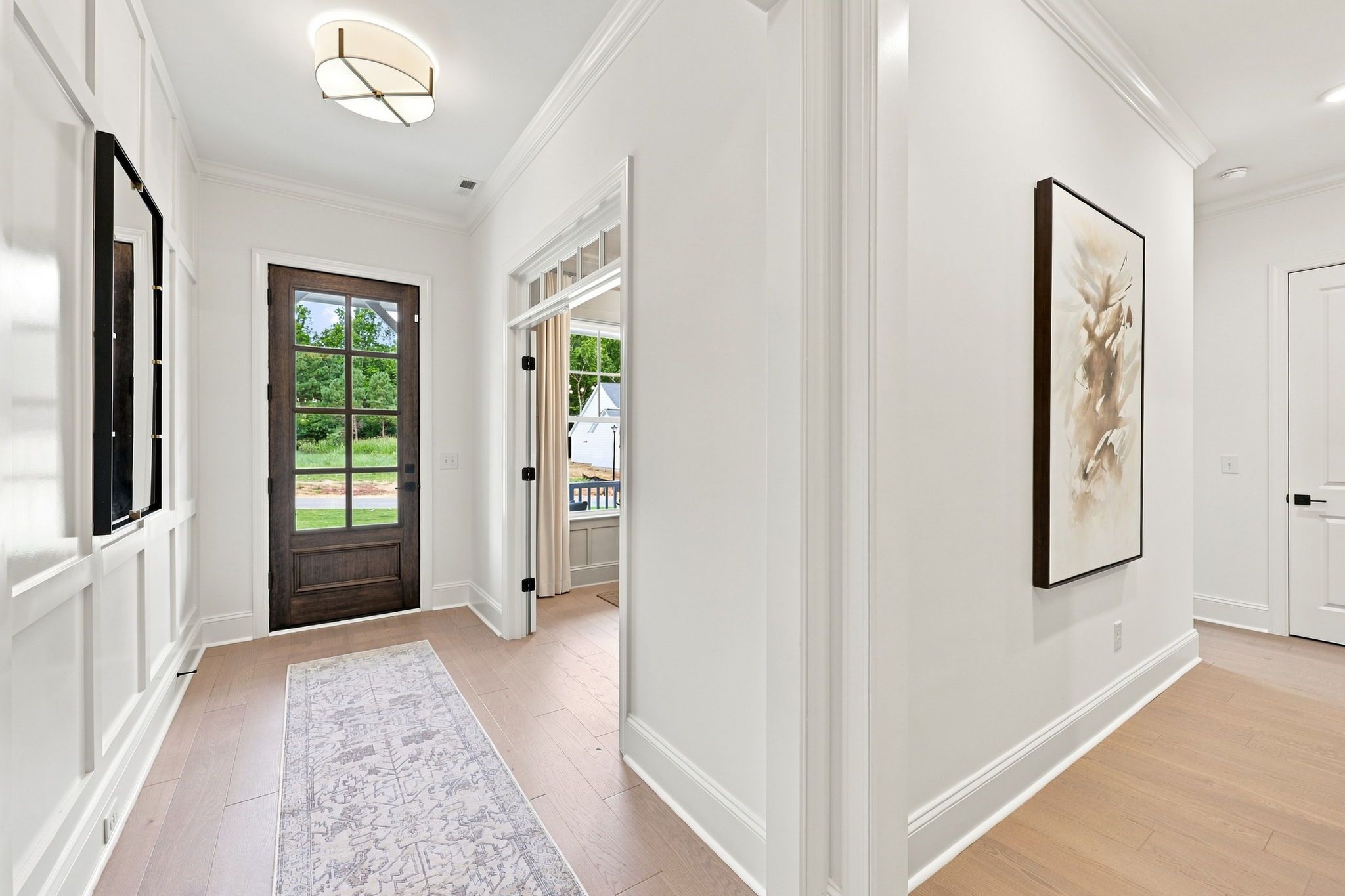 Bright foyer entrance in The Barrington C by Davidson Homes featuring white wainscoting, light wood floors, and glass door.