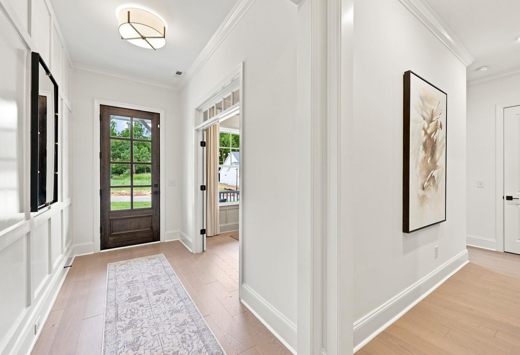 Bright, modern foyer in The Barrington by Davidson Homes featuring wood flooring, wainscoting, and a stained wood front door.