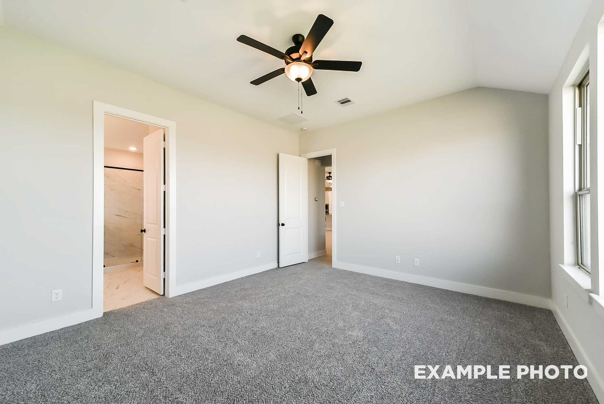 Bright bedroom with ceiling fan, gray carpet, en-suite bathroom door in Davidson Homes The Philip C, Rosharon, Texas