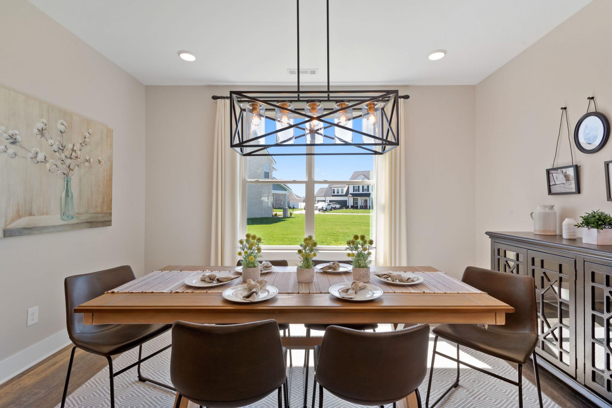Spacious dining room at Rivers Edge in Murfreesboro TN featuring wooden table with place settings, pendant light, and window view of green lawn