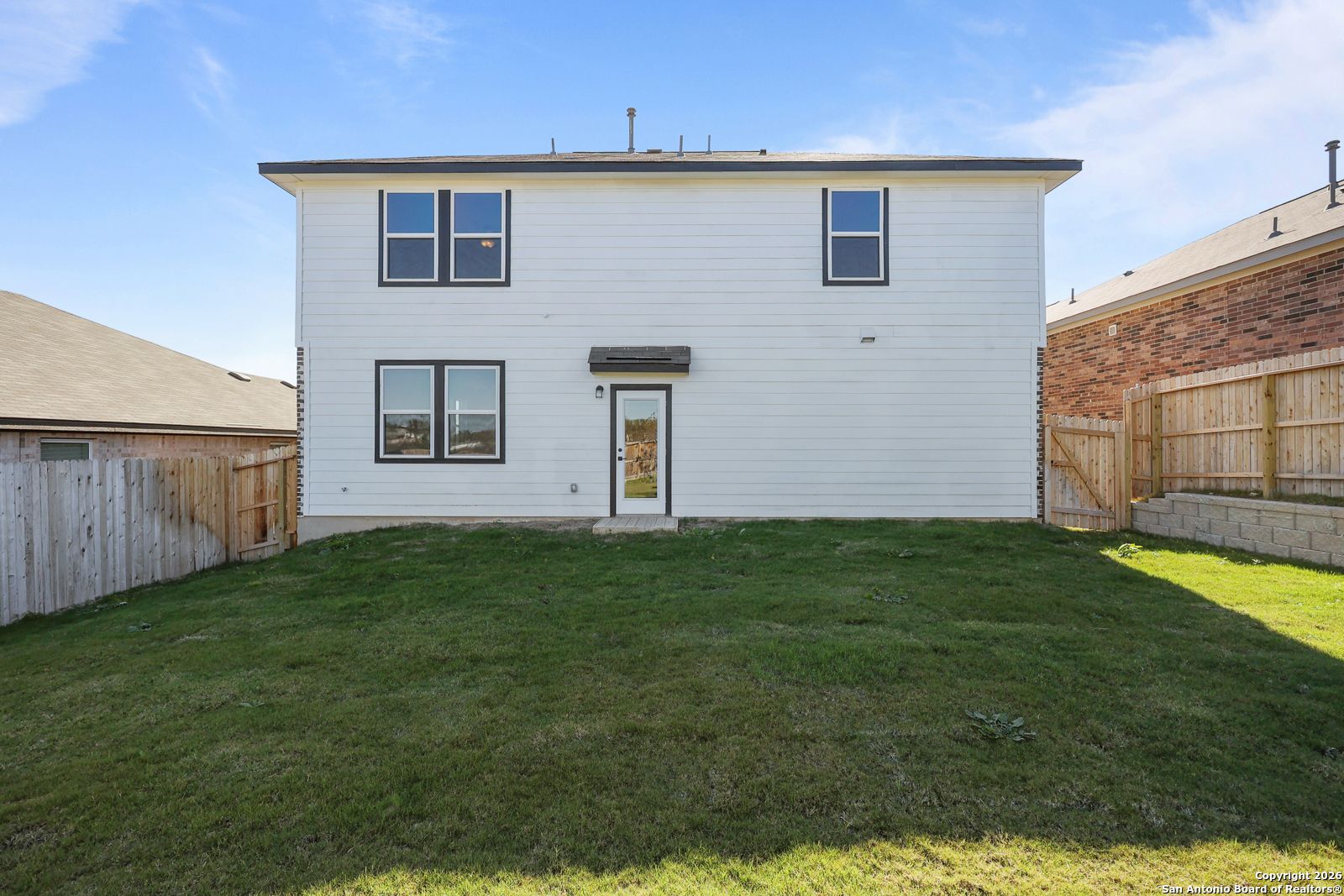 Rear view of two-story white 4-bedroom home with fenced grassy backyard and patio door, The Murray K in Comanche Ridge, San Antonio