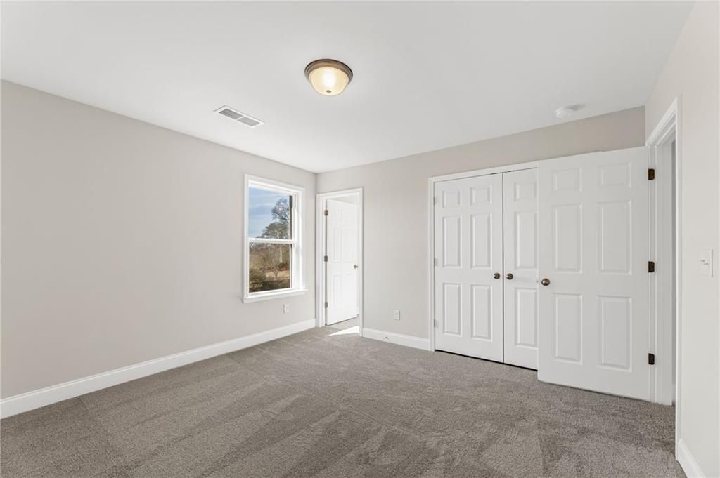 Bright bedroom with gray walls, carpeted floor, double-door closet, and window in Davidson Homes The Willow B, Hoschton, GA